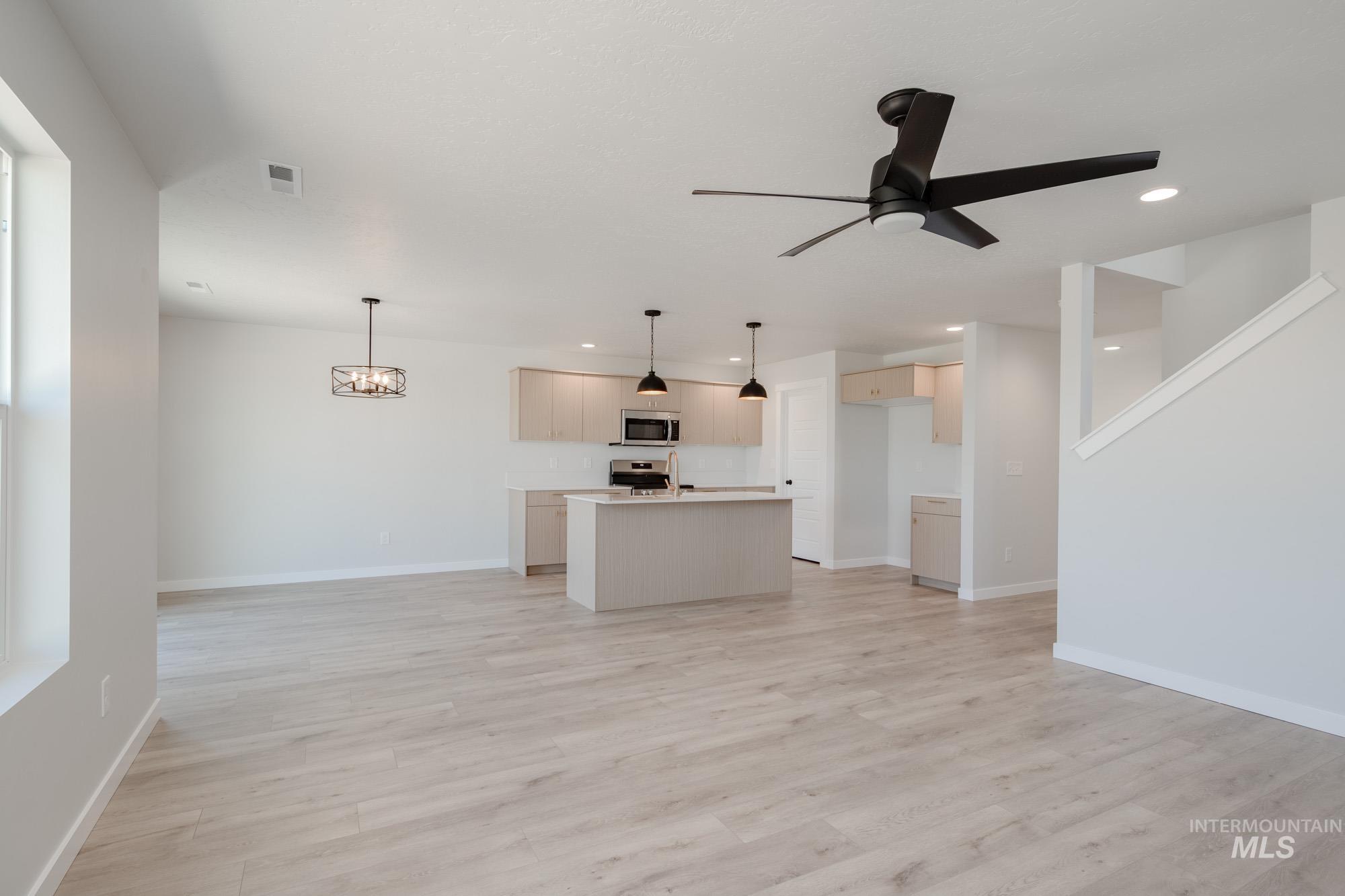 Unfurnished living room featuring a chandelier, light wood-style flooring, a ceiling fan, and recessed lighting