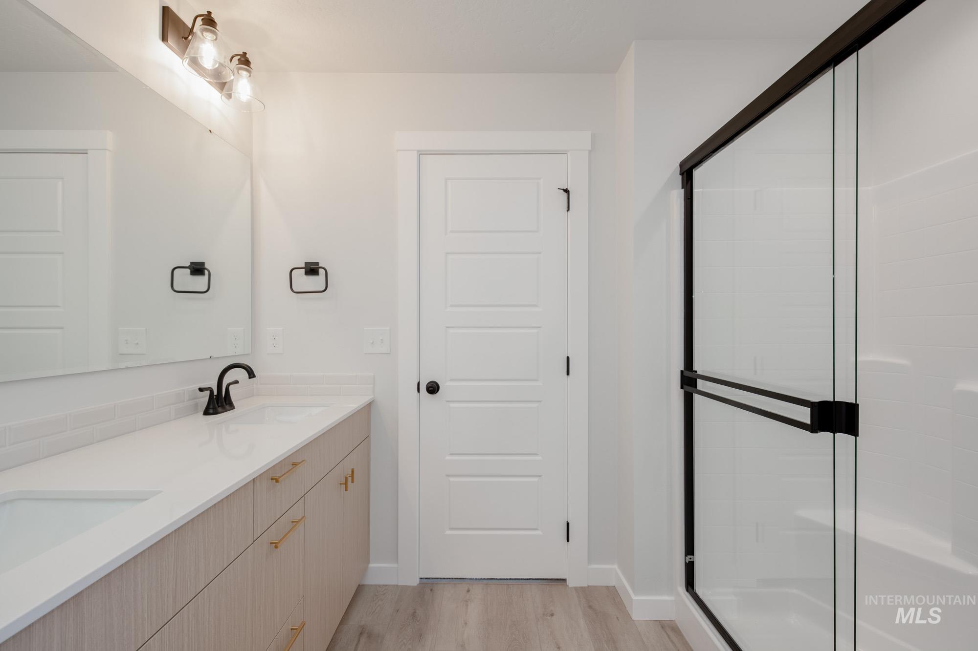 Full bath with double vanity, a stall shower, and light wood-style flooring