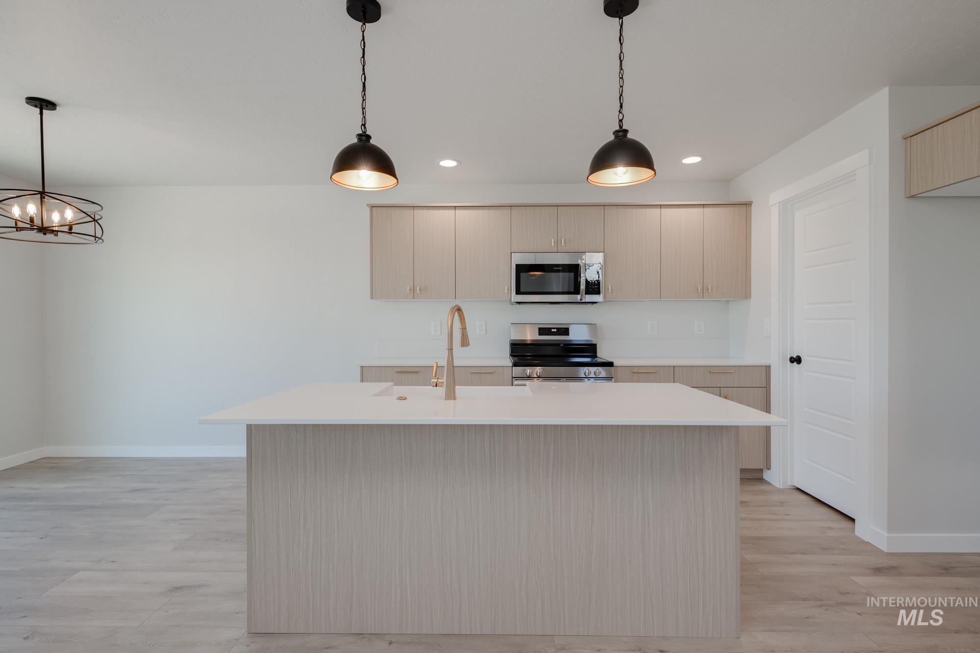 Kitchen featuring decorative light fixtures, stainless steel appliances, a kitchen island with sink, light wood-style floors, and light stone countertops