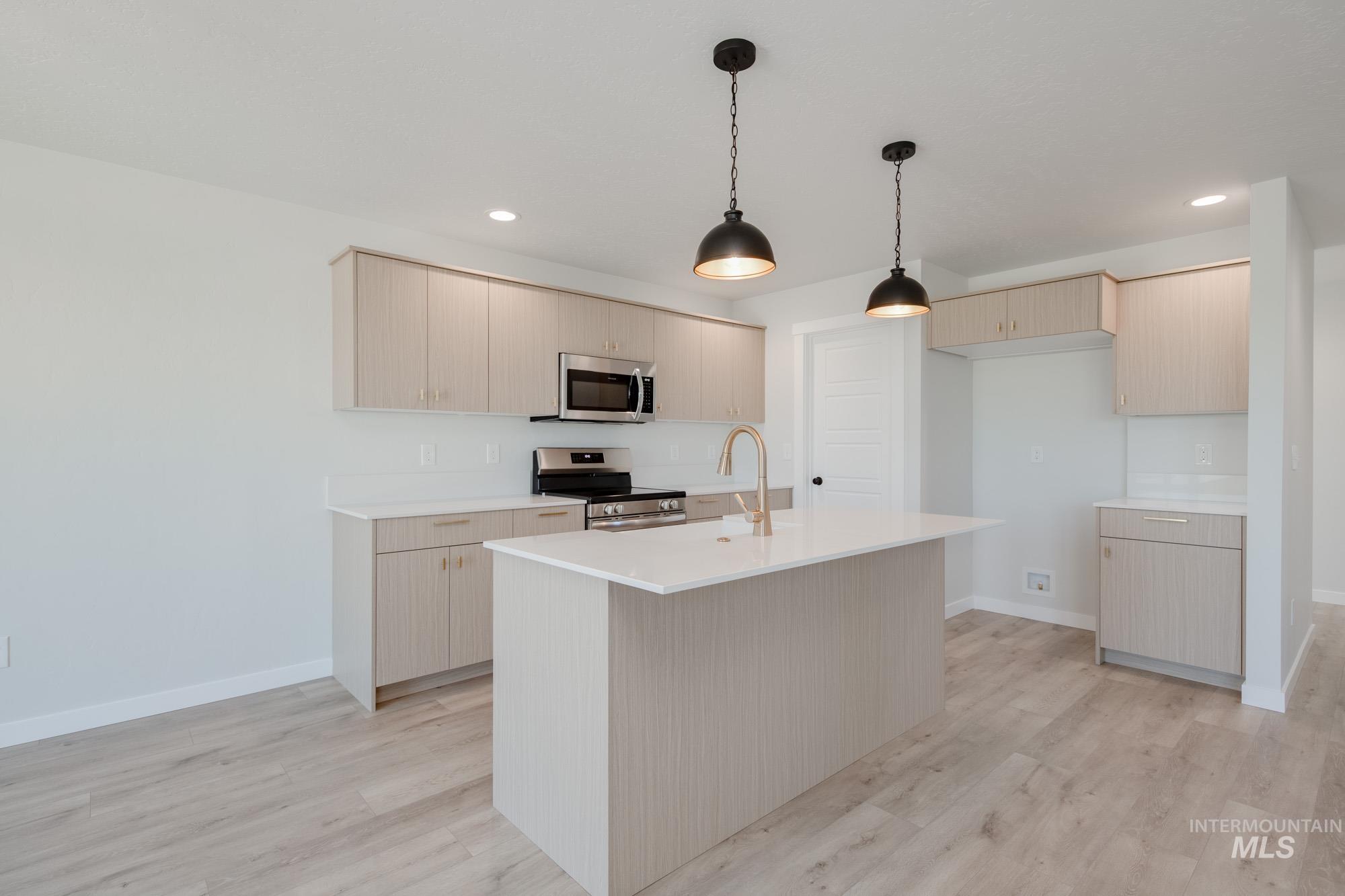 Kitchen featuring stainless steel appliances, hanging light fixtures, recessed lighting, light wood finished floors, and an island with sink