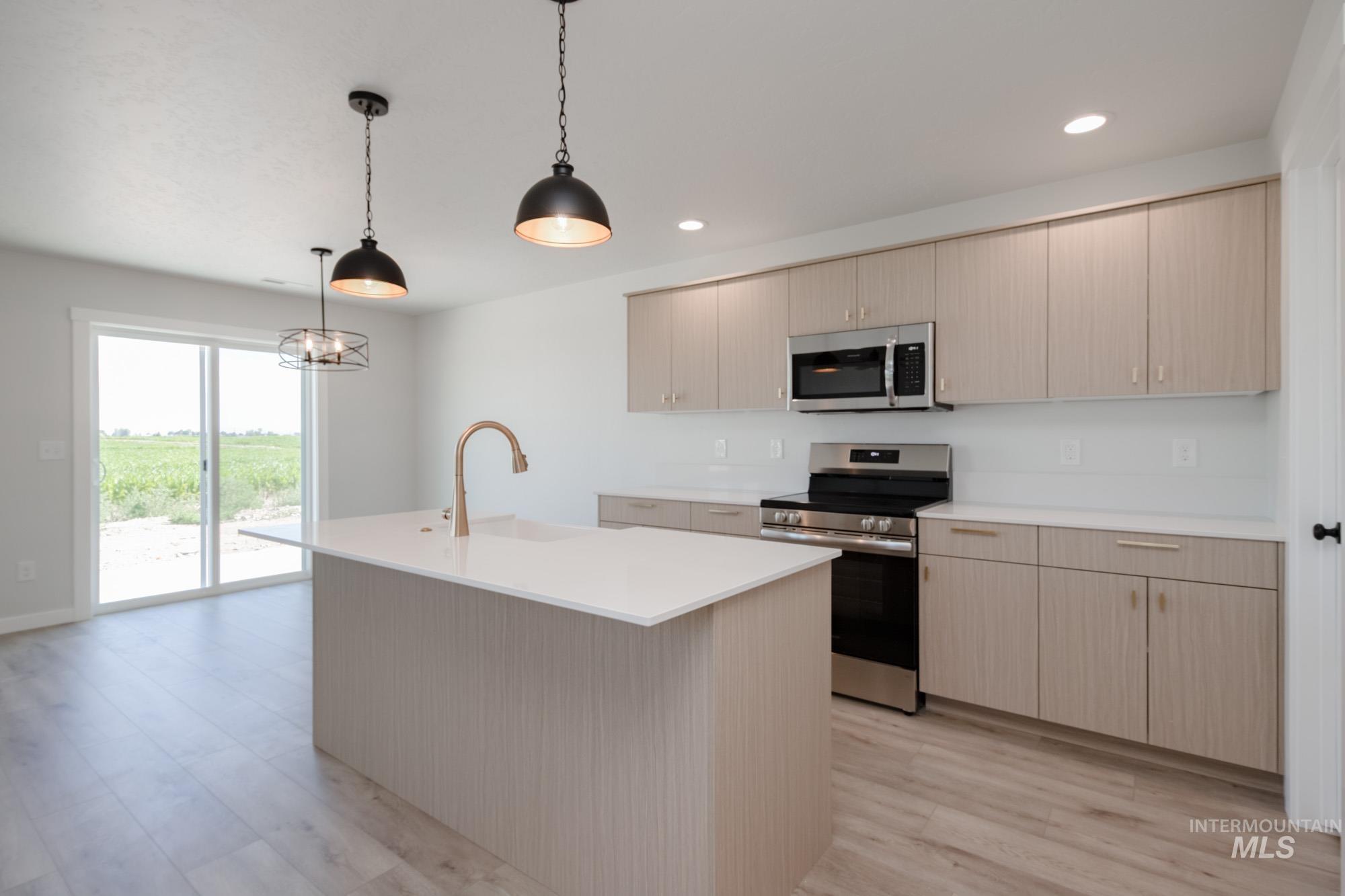 Kitchen featuring appliances with stainless steel finishes, hanging light fixtures, recessed lighting, an island with sink, and light wood finished floors