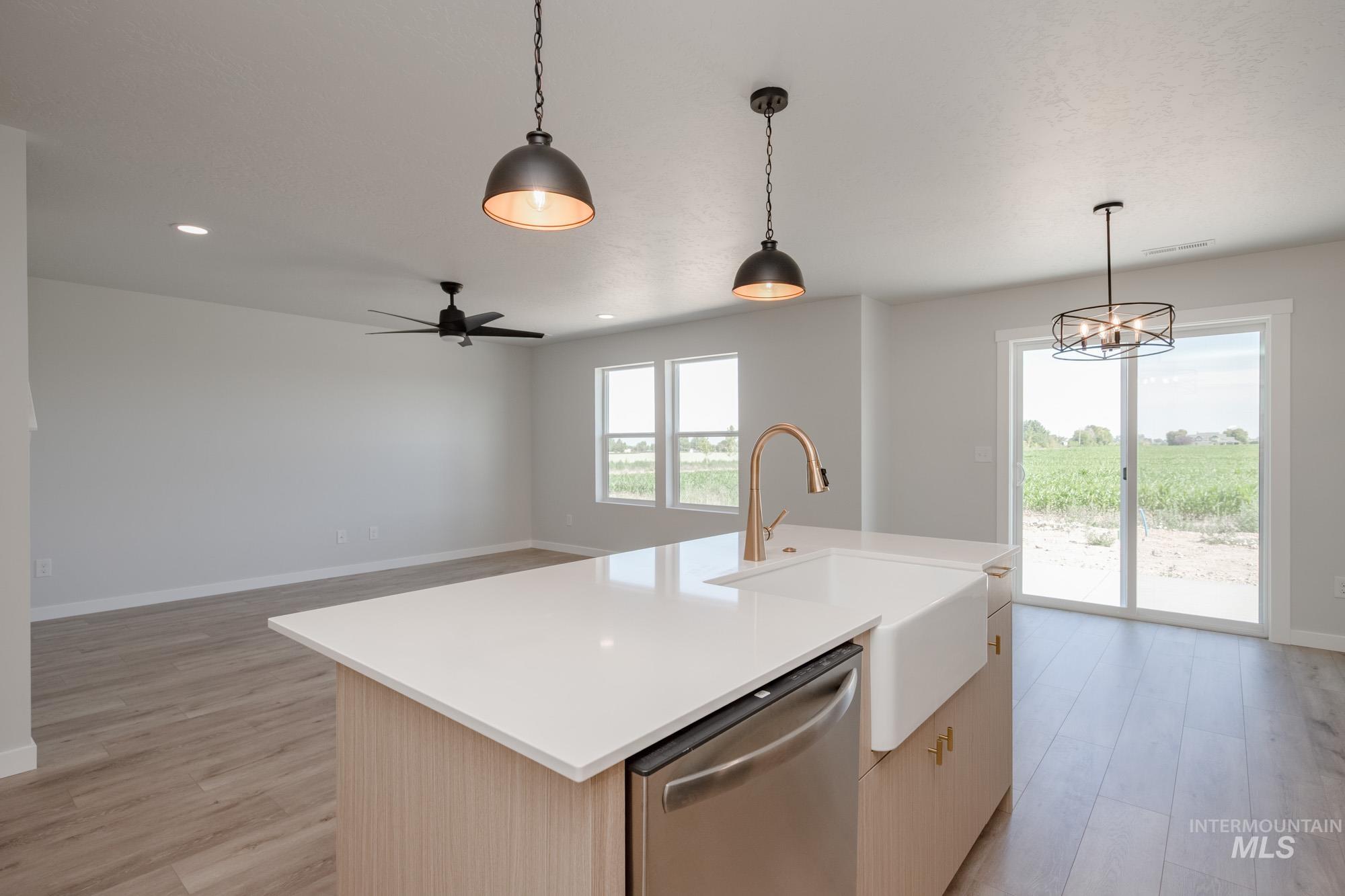 Kitchen with dishwasher, light brown cabinets, hanging light fixtures, a center island with sink, and open floor plan