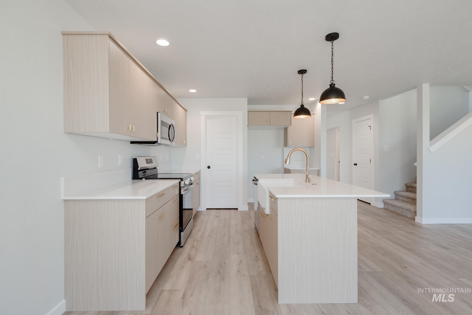 Kitchen featuring stainless steel appliances, decorative light fixtures, a center island with sink, light wood finished floors, and light stone counters