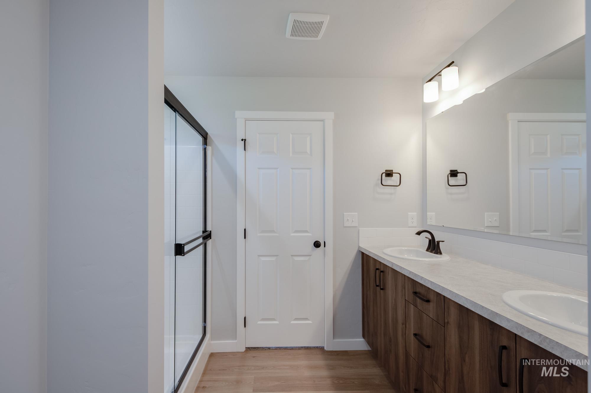 Bathroom featuring double vanity, a stall shower, and light wood finished floors