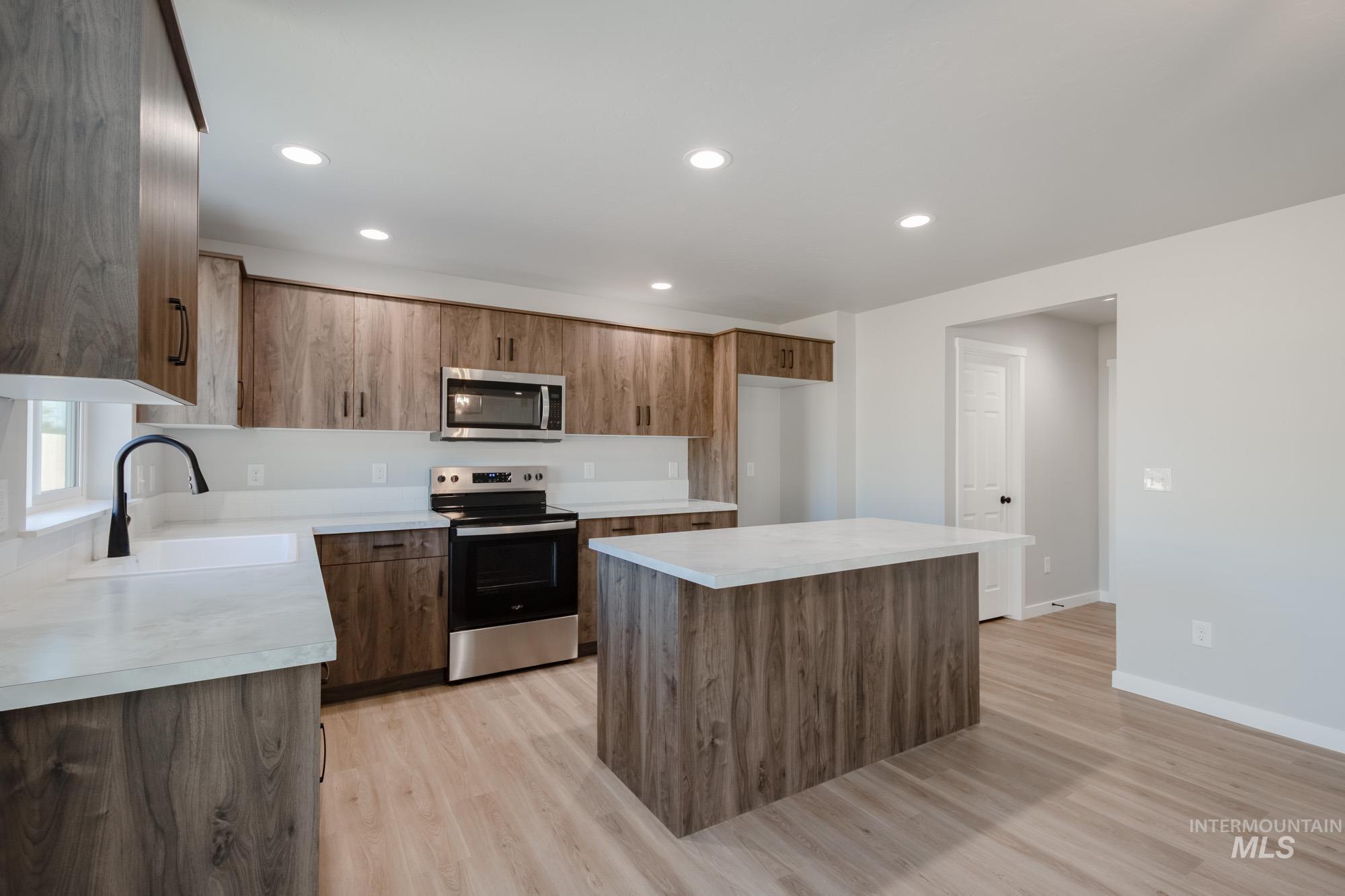 Kitchen featuring appliances with stainless steel finishes, a center island, recessed lighting, light countertops, and light wood-style floors
