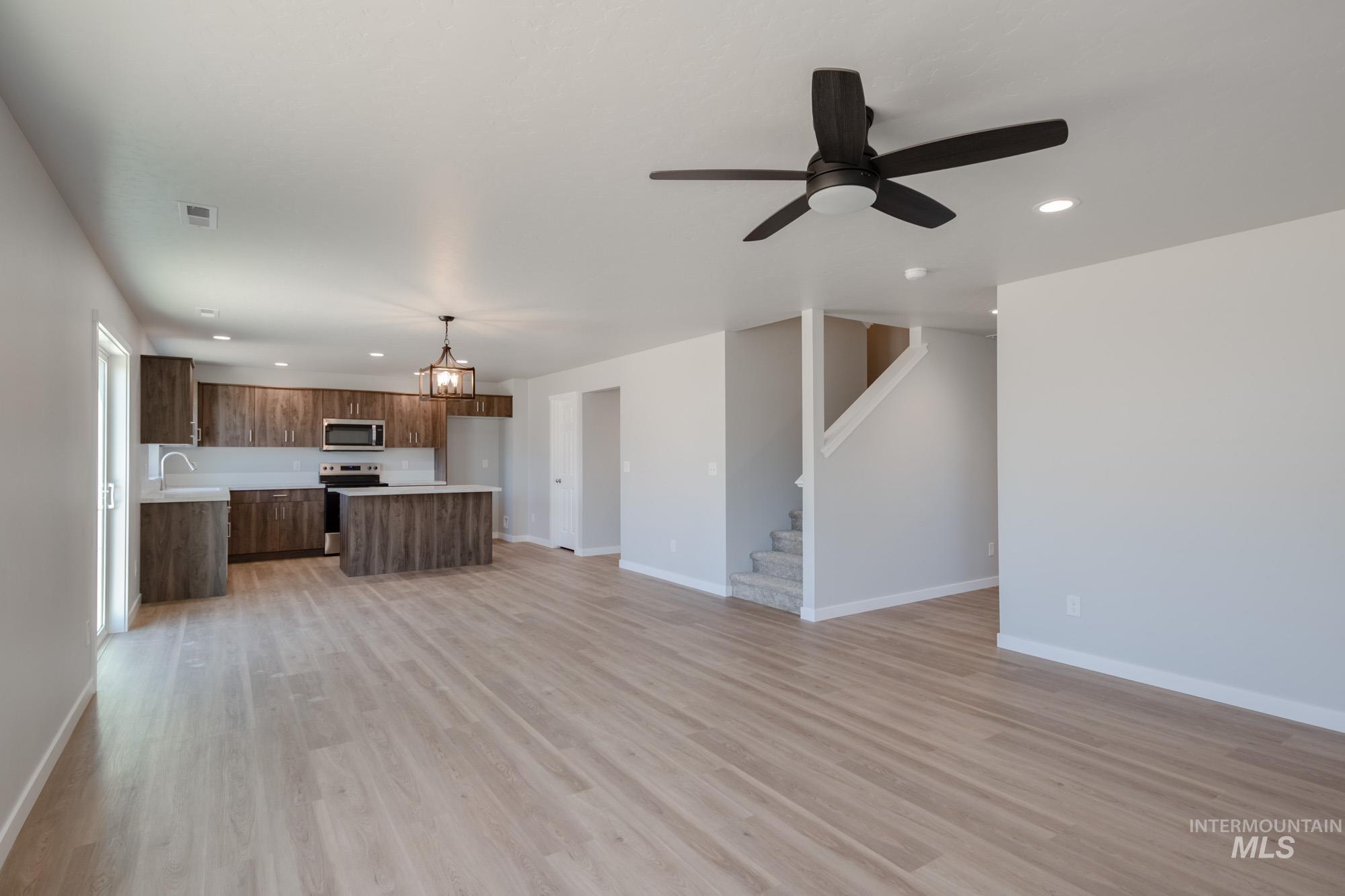 Unfurnished living room featuring recessed lighting, a ceiling fan, a chandelier, light wood-type flooring, and stairs