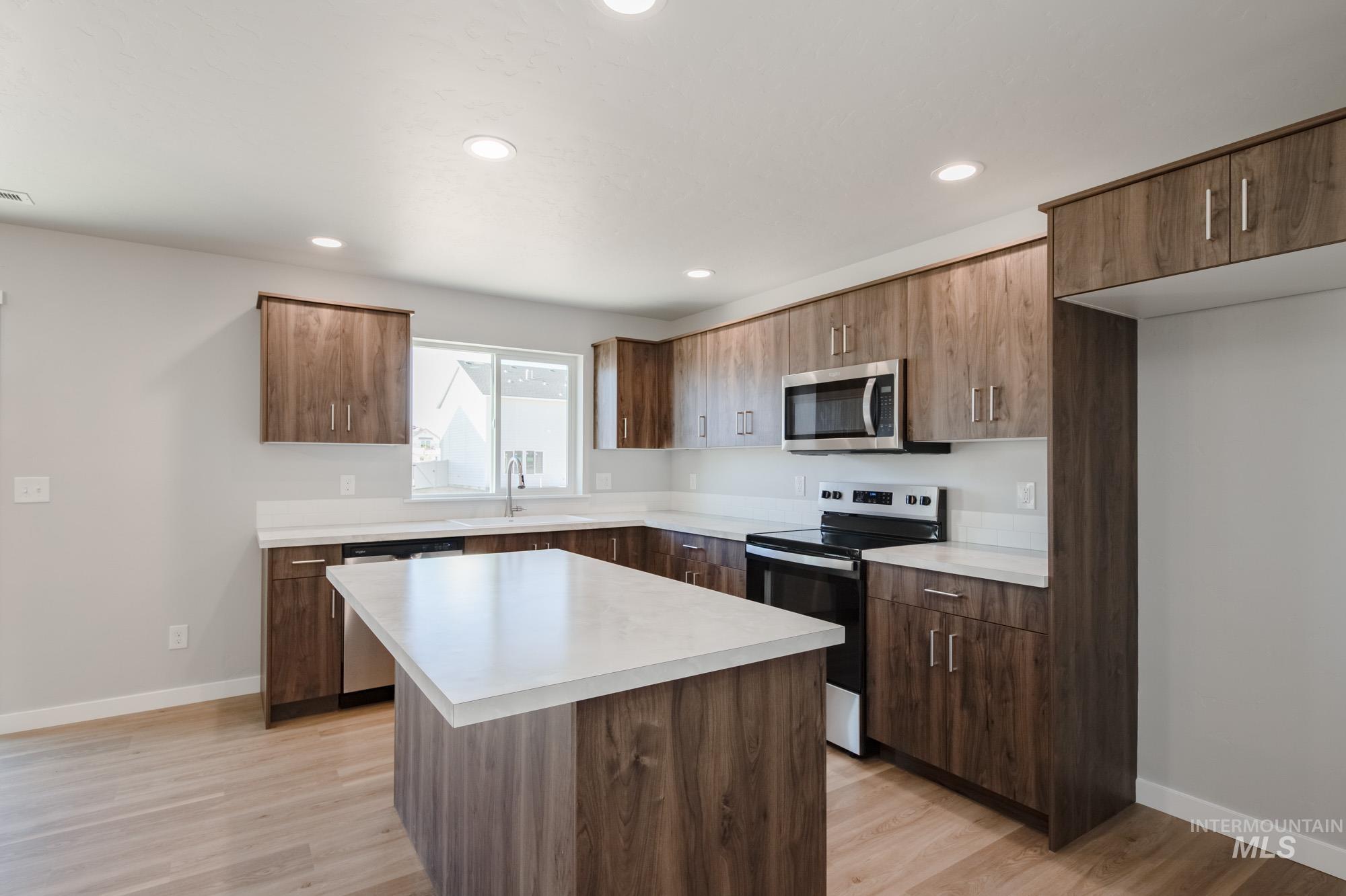 Kitchen featuring appliances with stainless steel finishes, light countertops, a center island, light wood-style floors, and recessed lighting