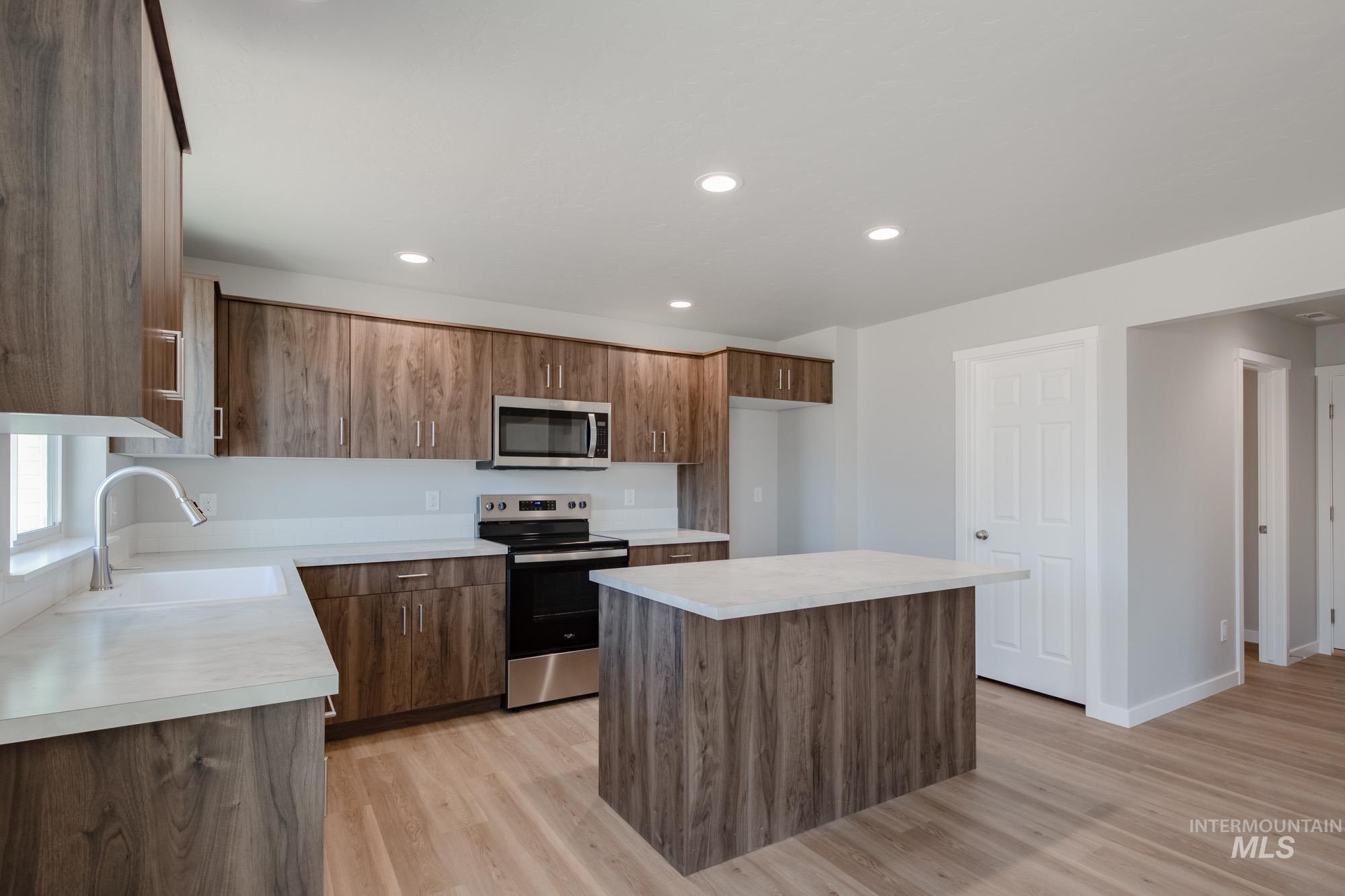 Kitchen with a kitchen island, stainless steel appliances, light countertops, brown cabinets, and recessed lighting
