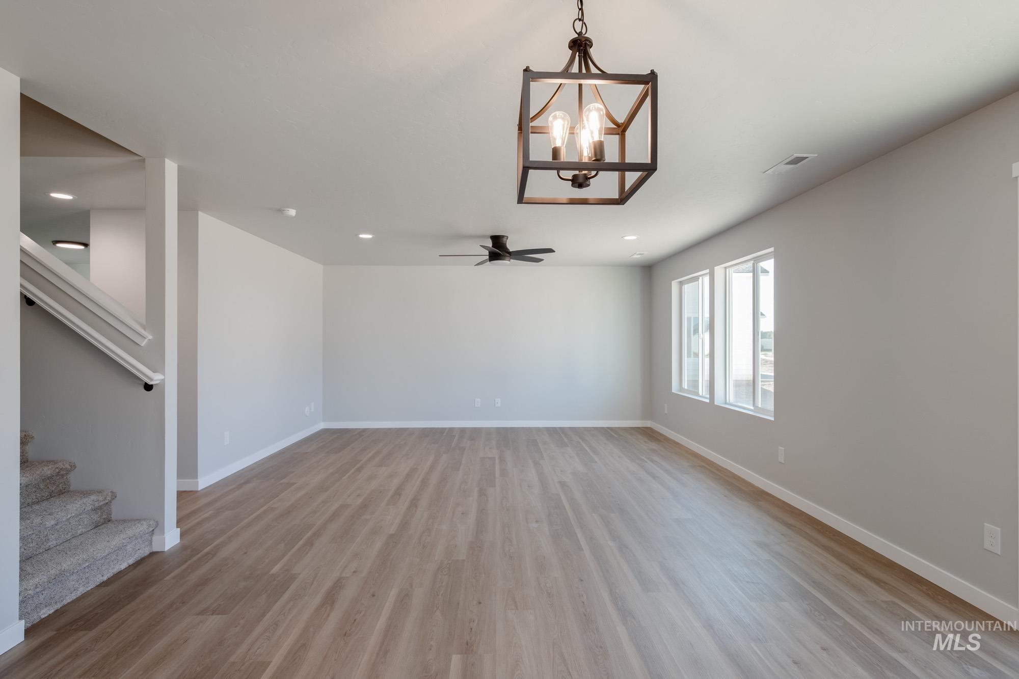 Unfurnished living room featuring a chandelier, light wood-type flooring, stairway, ceiling fan, and recessed lighting