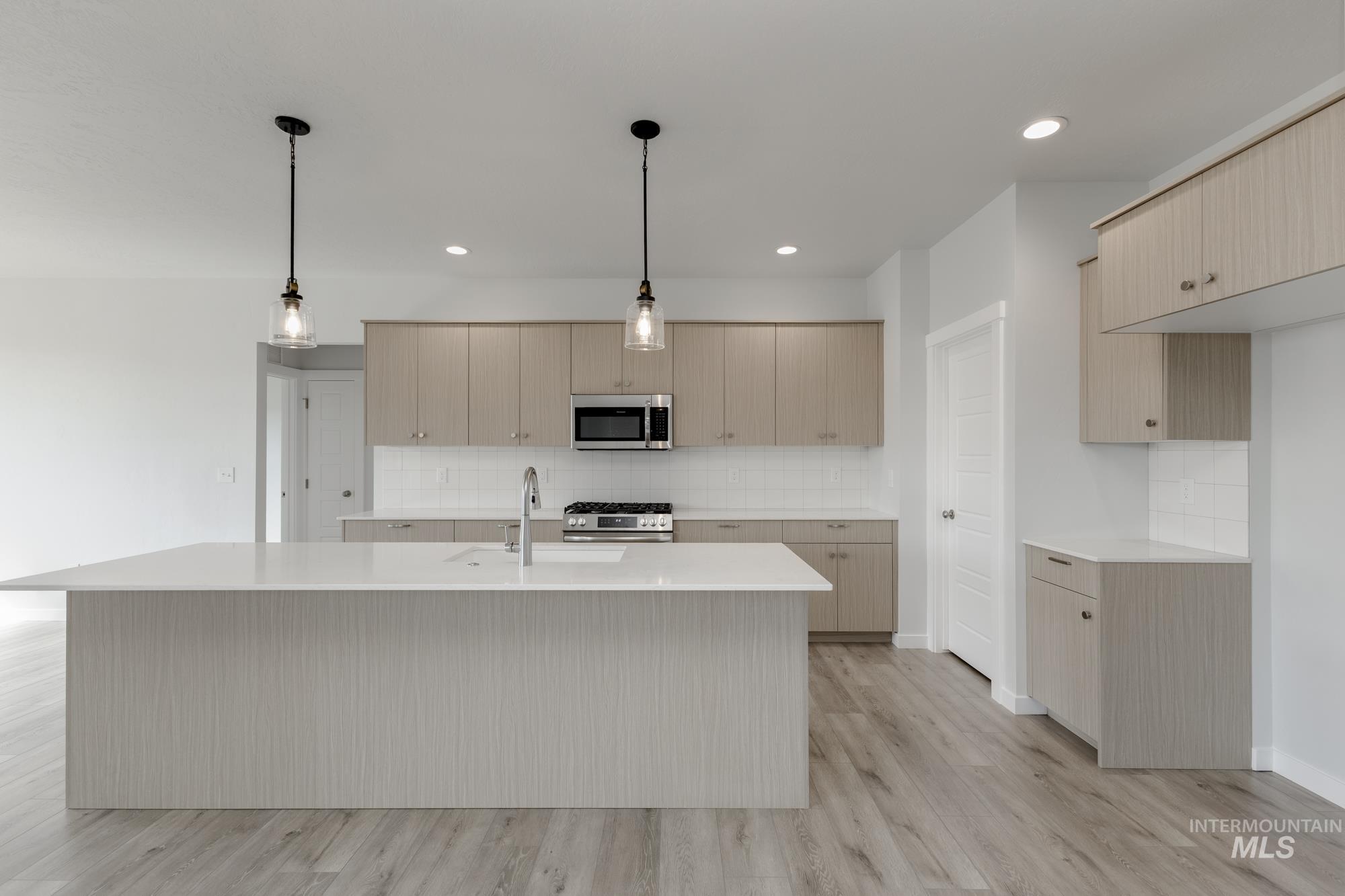 Kitchen with tasteful backsplash, a kitchen island with sink, light wood-style flooring, hanging light fixtures, and recessed lighting