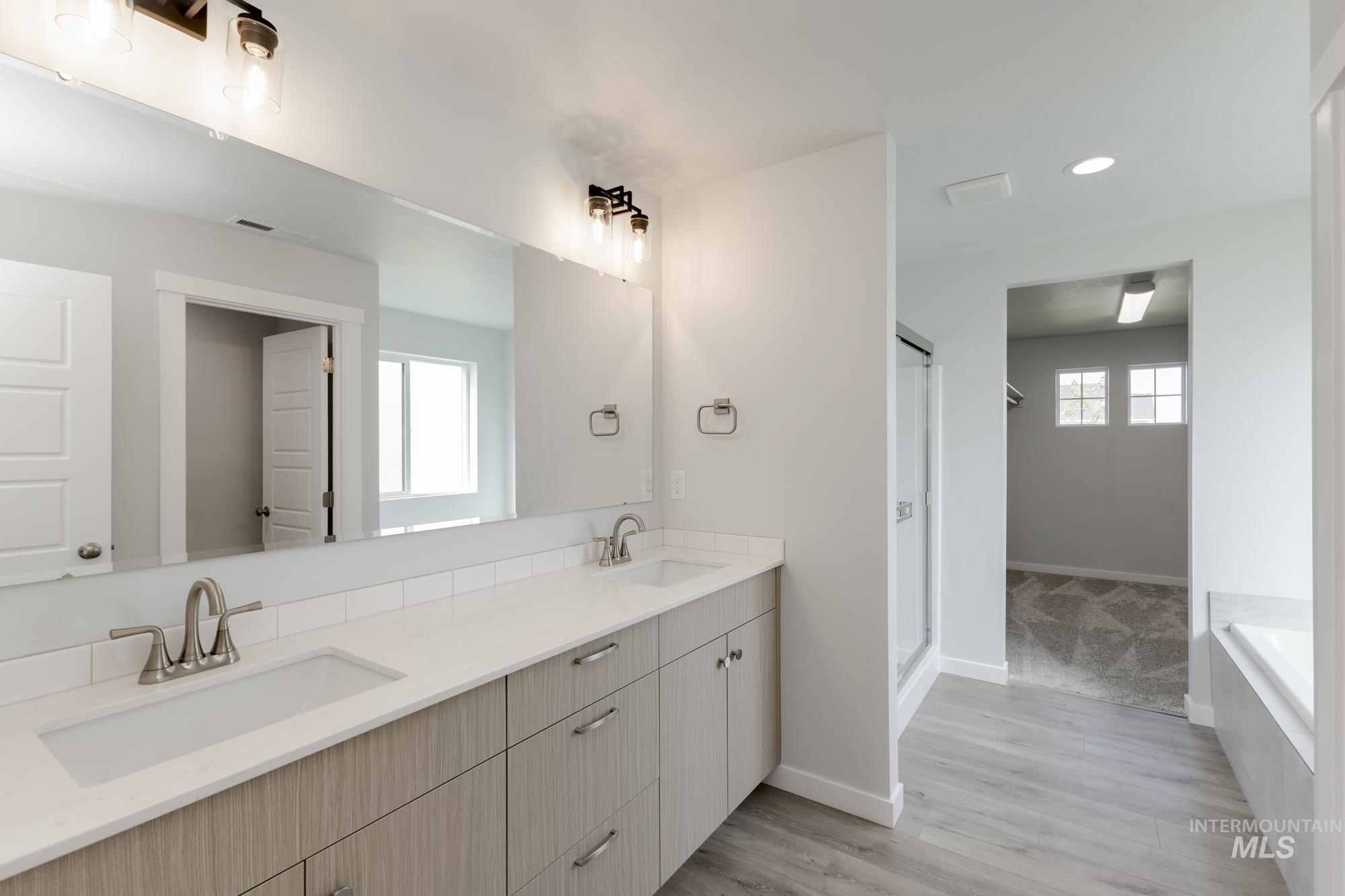 Bathroom featuring healthy amount of natural light, double vanity, light wood-style floors, recessed lighting, and a garden tub