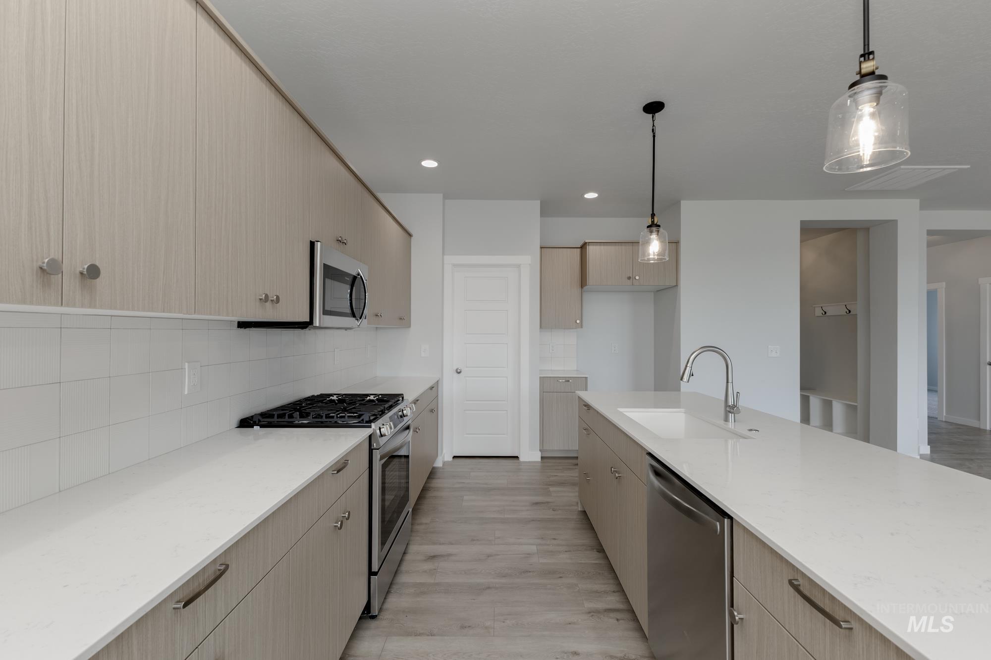Kitchen featuring stainless steel appliances, decorative light fixtures, light stone countertops, light brown cabinetry, and recessed lighting