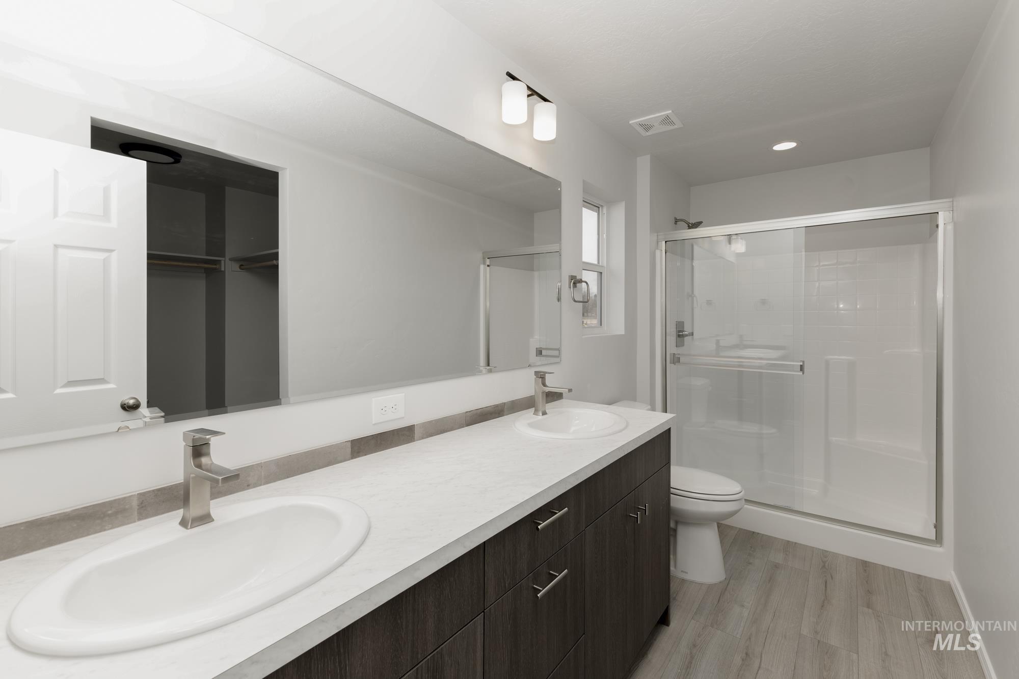 Full bath featuring double vanity, a stall shower, and light wood-style floors