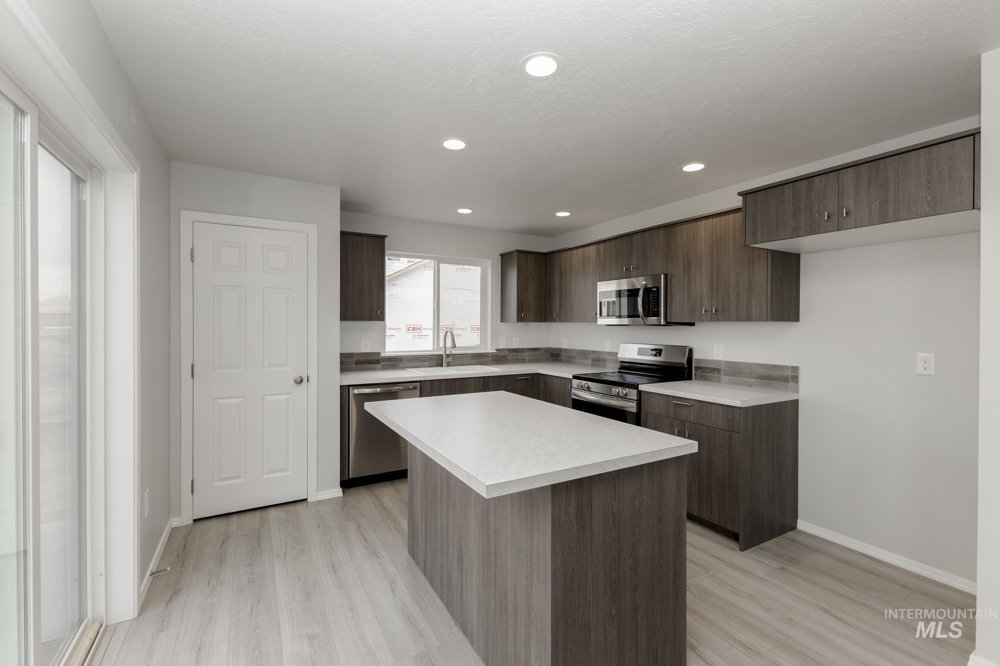 Kitchen with appliances with stainless steel finishes, light countertops, dark brown cabinetry, a center island, and modern cabinets