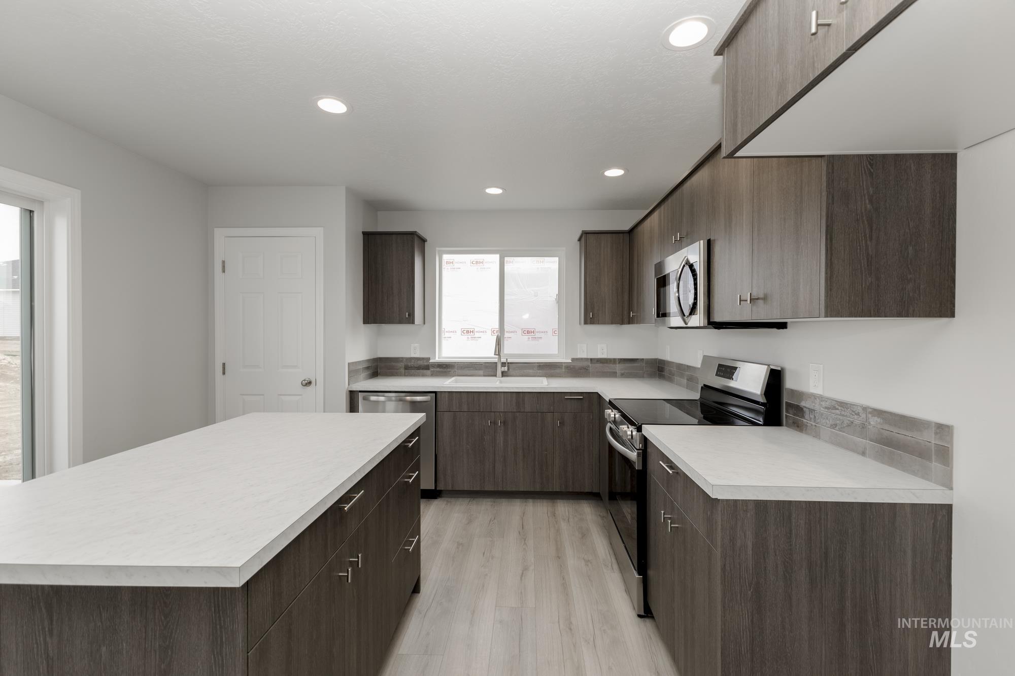 Kitchen featuring stainless steel appliances, light countertops, a kitchen island, dark brown cabinets, and recessed lighting