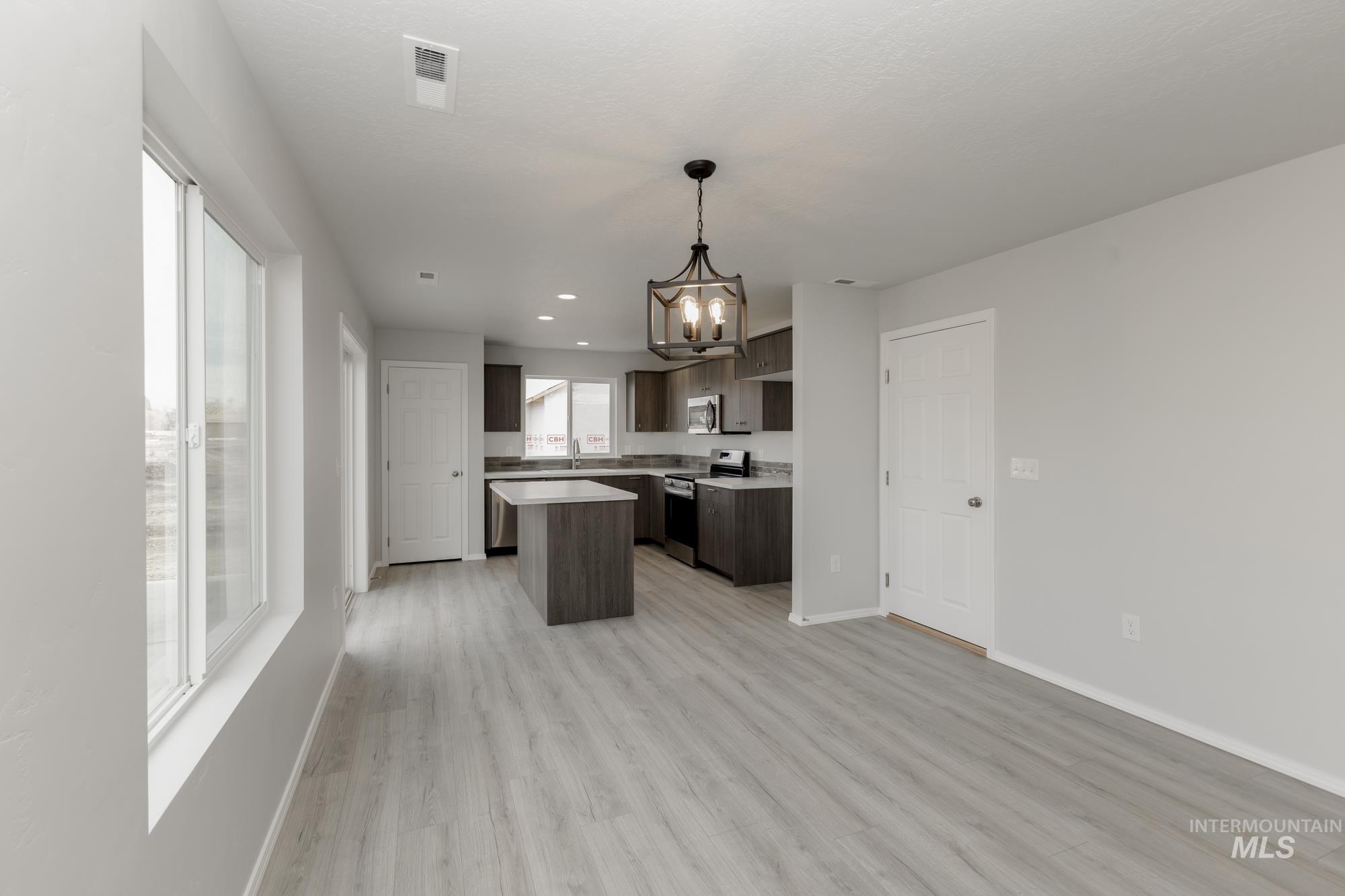 Kitchen with light countertops, a chandelier, appliances with stainless steel finishes, dark brown cabinets, and open floor plan