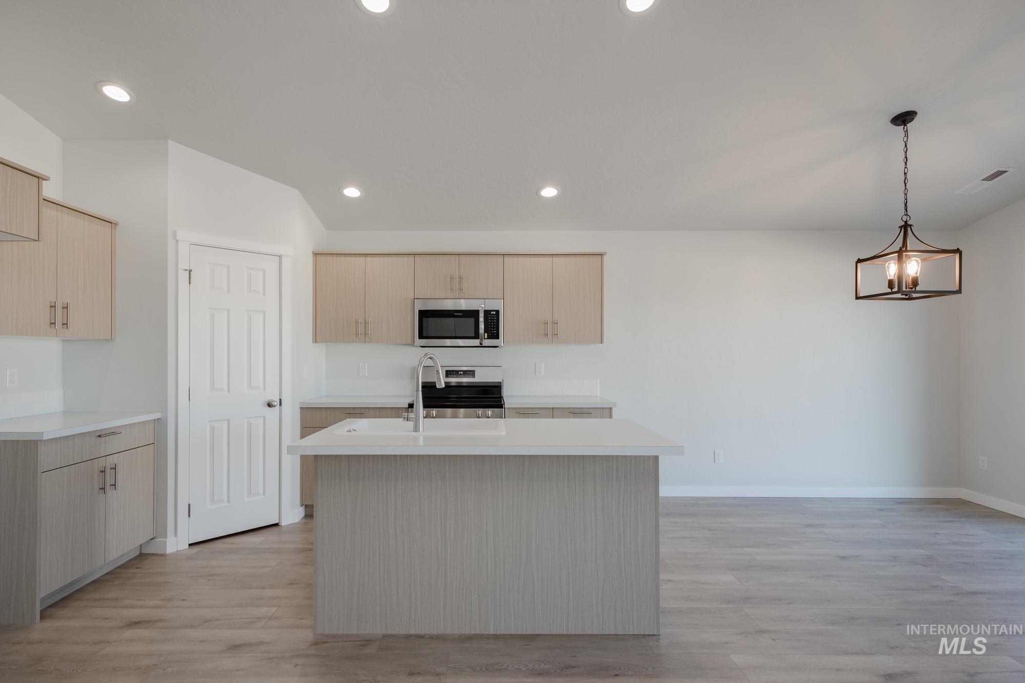 Kitchen featuring decorative light fixtures, a center island with sink, recessed lighting, light brown cabinetry, and light wood-type flooring
