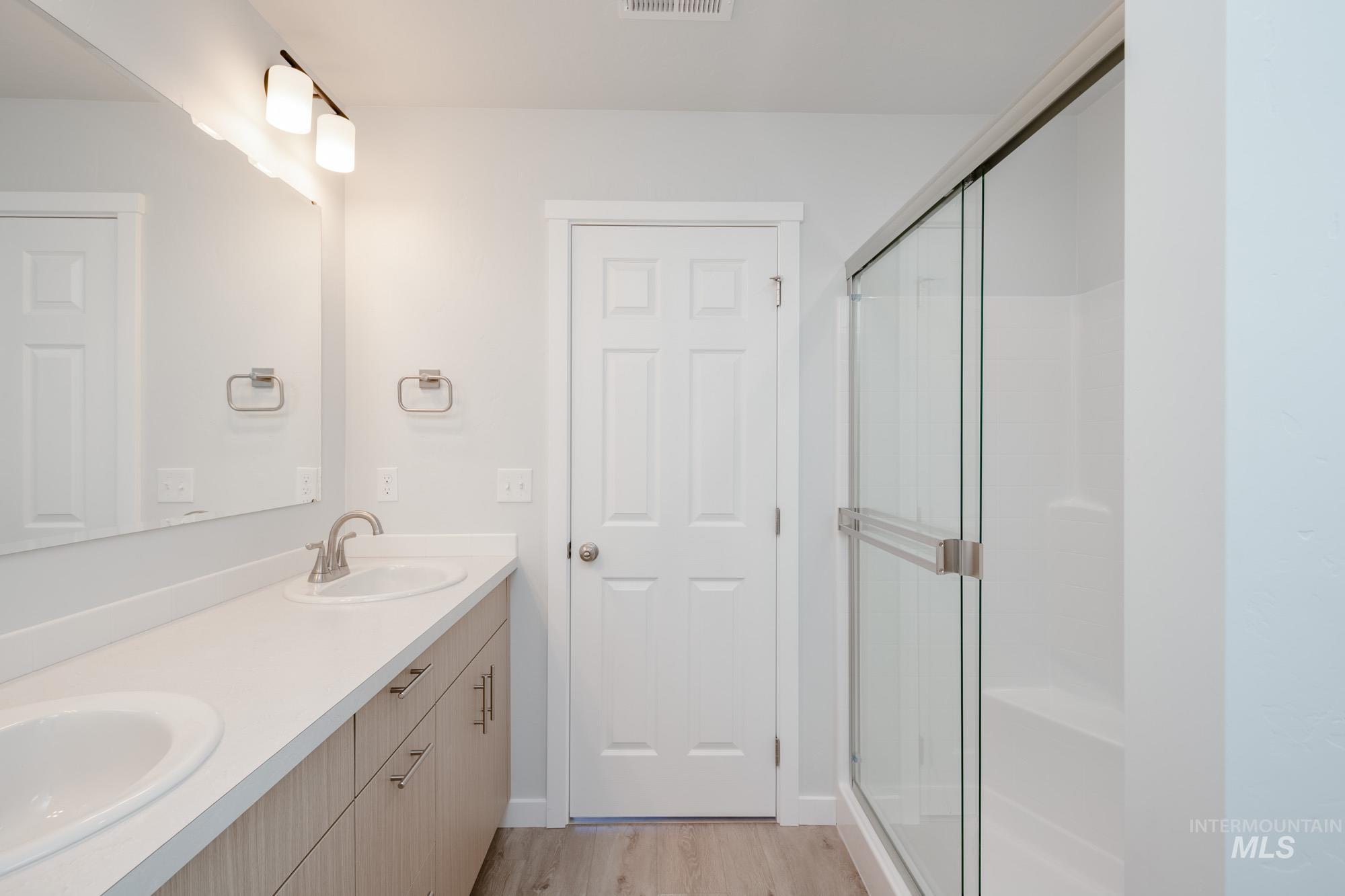 Full bath with double vanity, light wood-style floors, and a stall shower