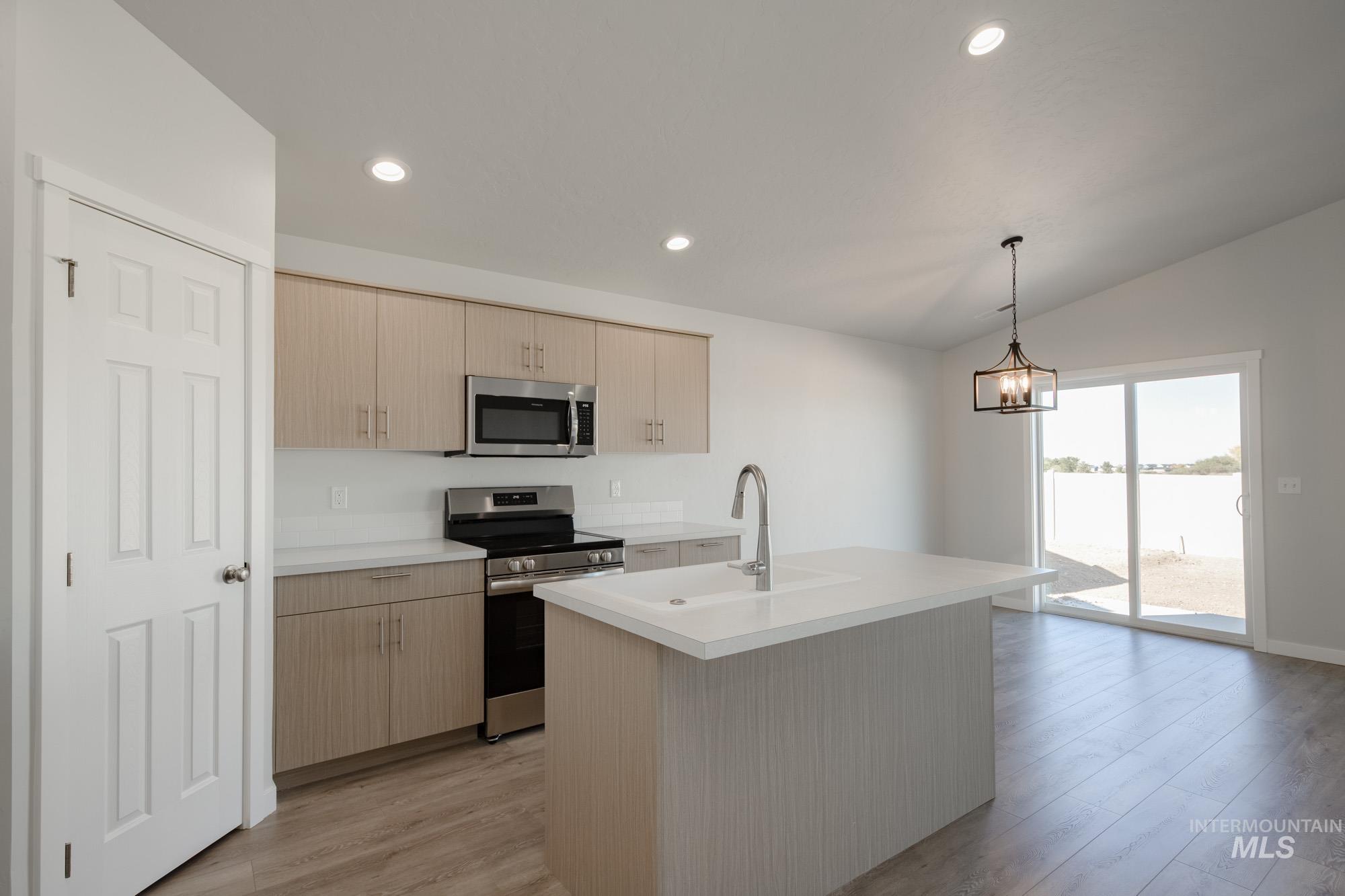 Kitchen featuring stainless steel appliances, light countertops, light brown cabinetry, pendant lighting, and a kitchen island with sink