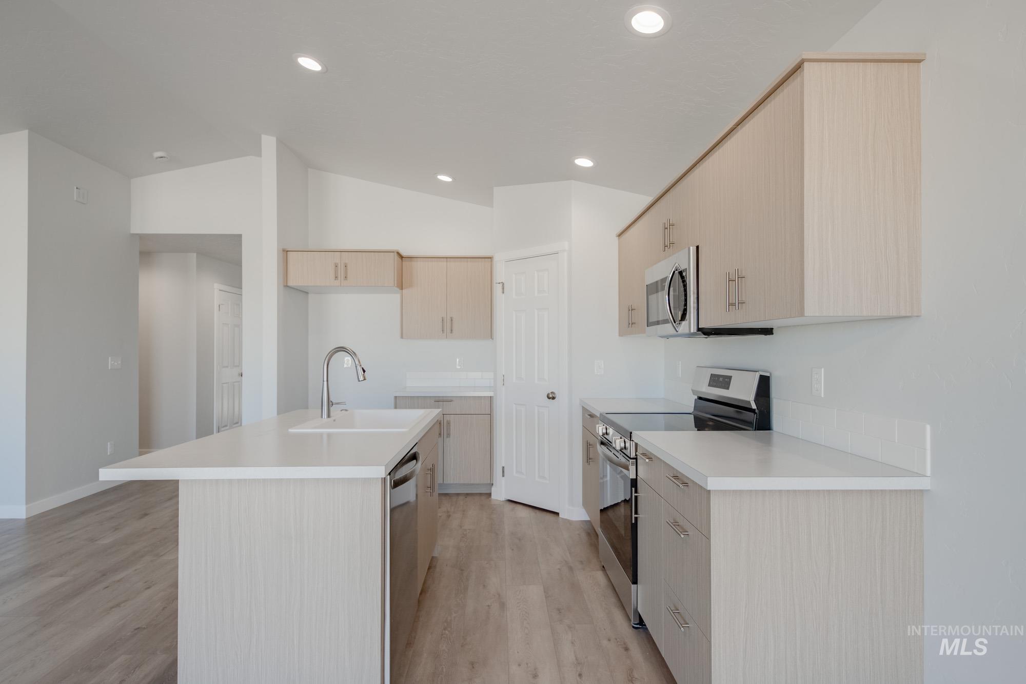 Kitchen with light brown cabinetry, appliances with stainless steel finishes, light countertops, light wood-style floors, and vaulted ceiling