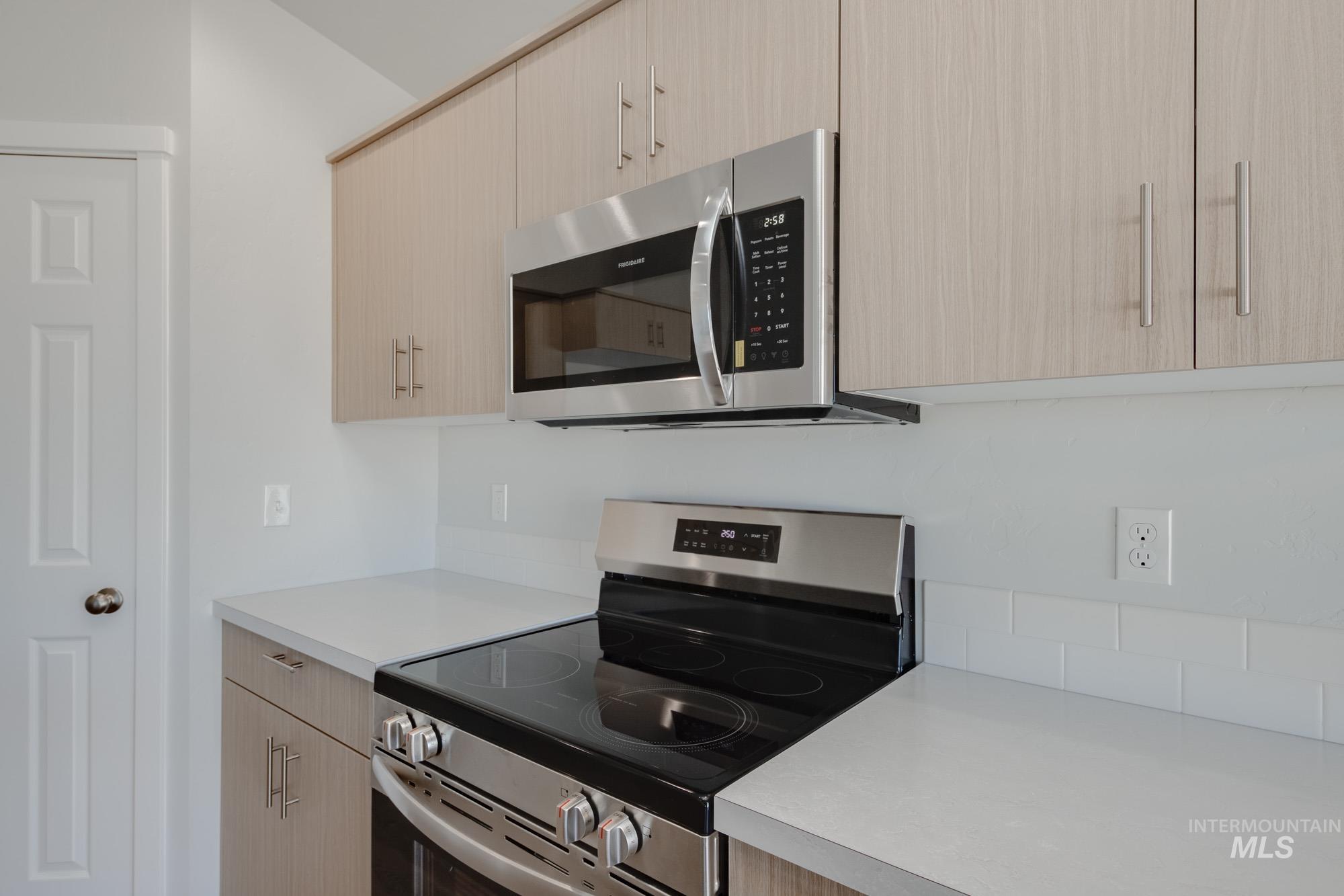 Kitchen with stainless steel appliances, light countertops, light brown cabinets, and modern cabinets