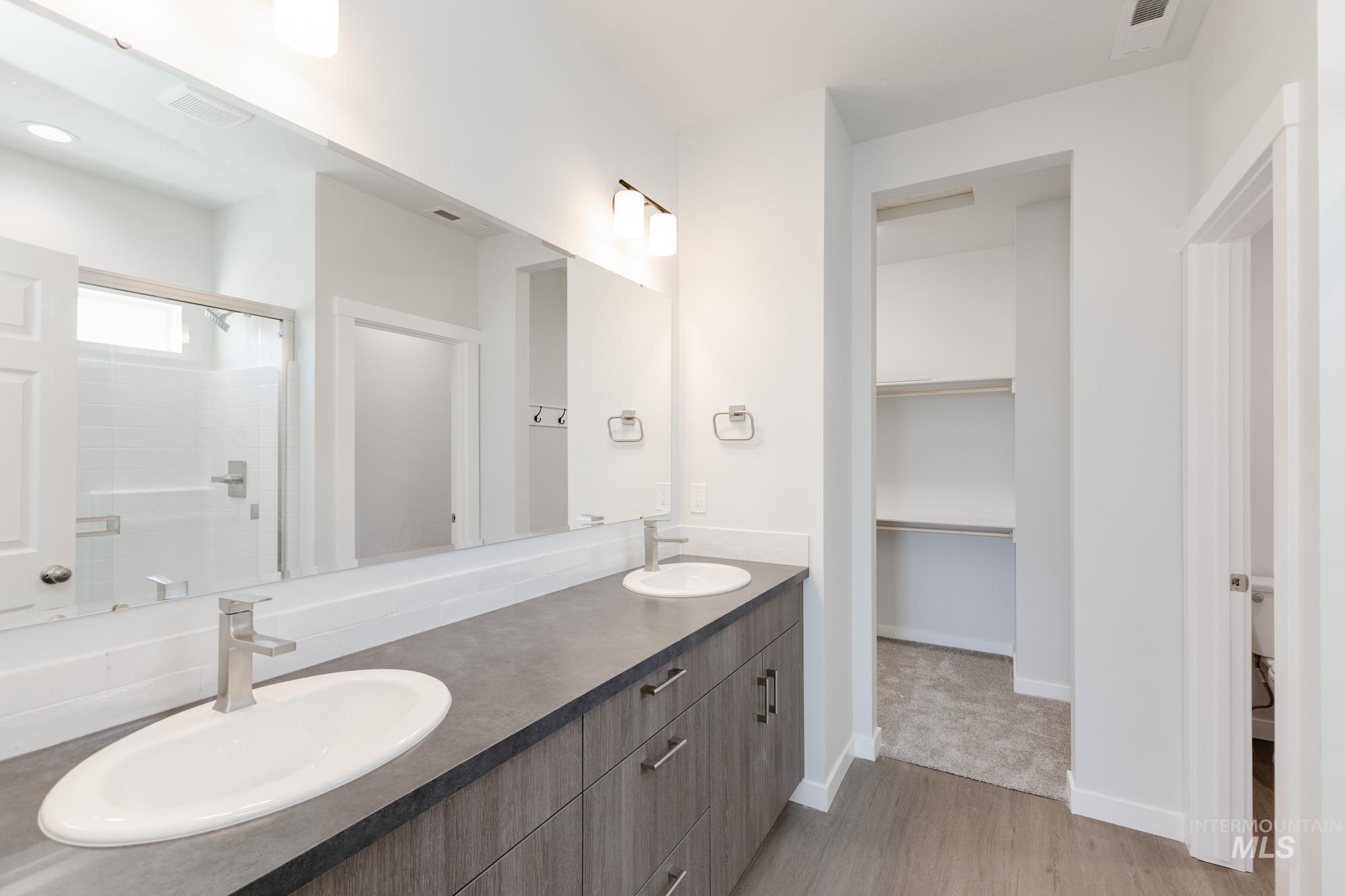 Full bath featuring double vanity, a shower stall, light wood finished floors, and a walk in closet