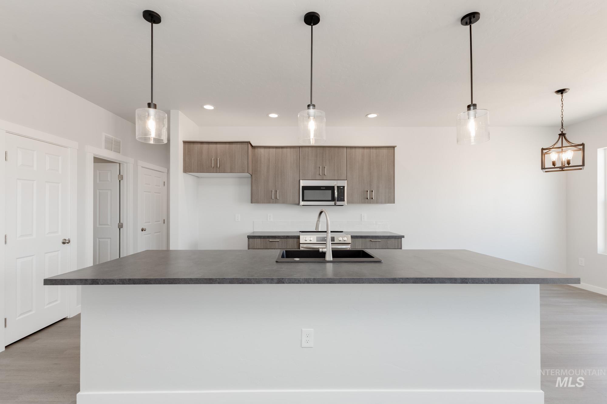 Kitchen with light wood-type flooring, decorative light fixtures, stainless steel microwave, and recessed lighting