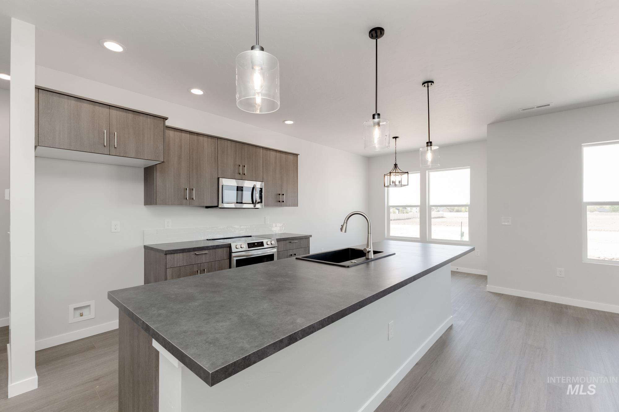 Kitchen with hanging light fixtures, appliances with stainless steel finishes, recessed lighting, a kitchen island with sink, and modern cabinets