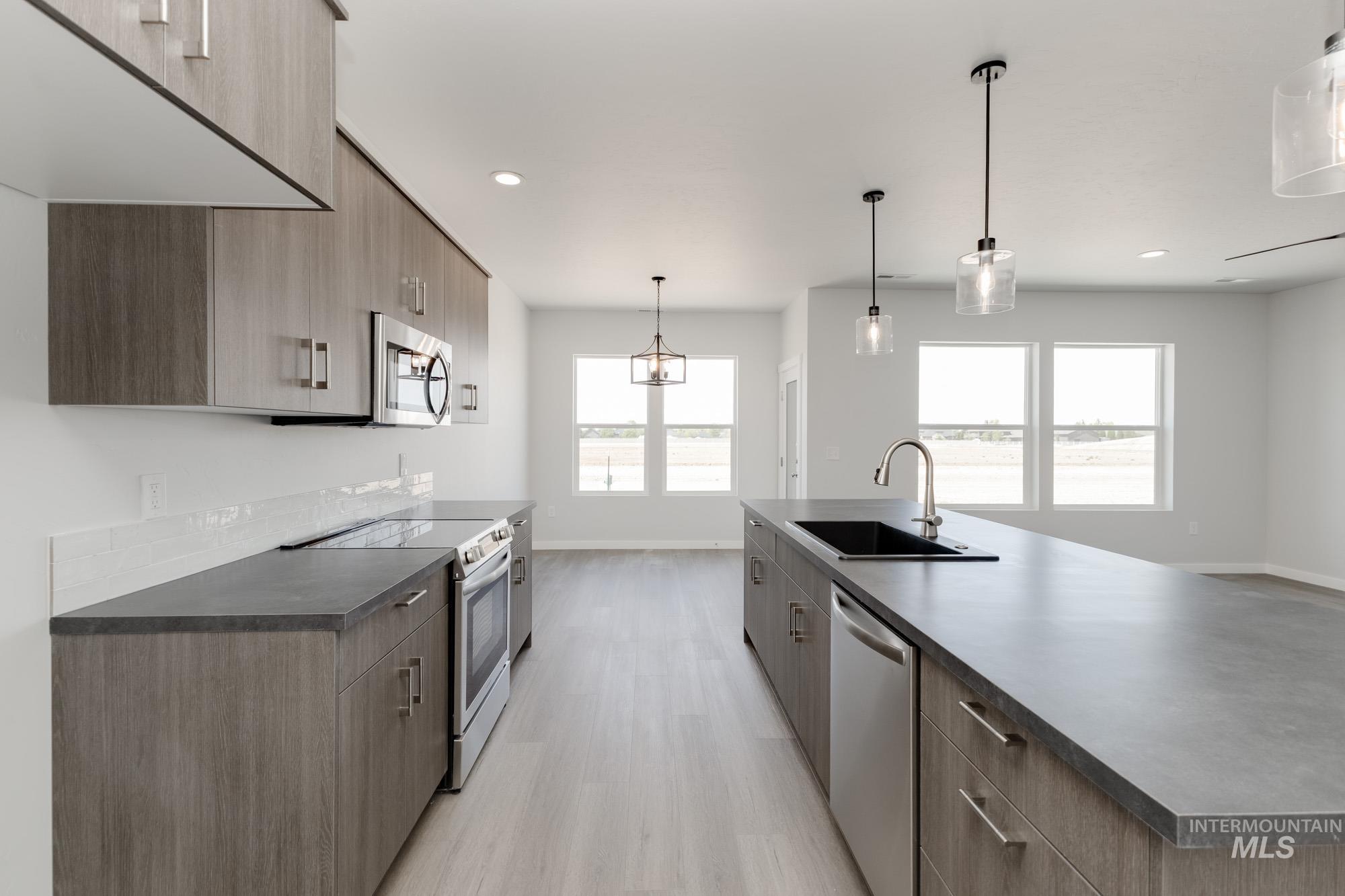 Kitchen with dark countertops, modern cabinets, appliances with stainless steel finishes, pendant lighting, and recessed lighting