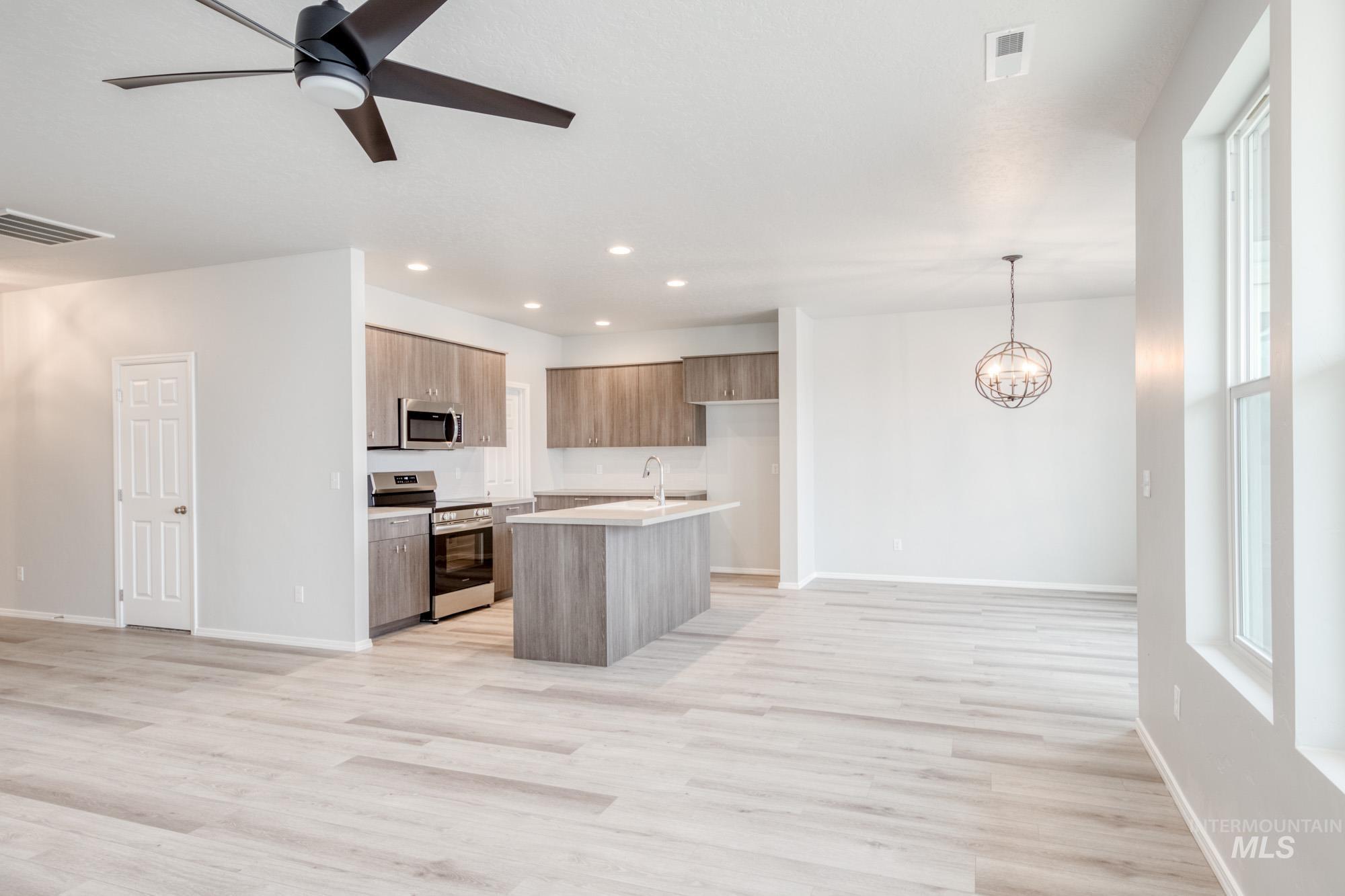 Kitchen with open floor plan, appliances with stainless steel finishes, a kitchen island with sink, a chandelier, and pendant lighting