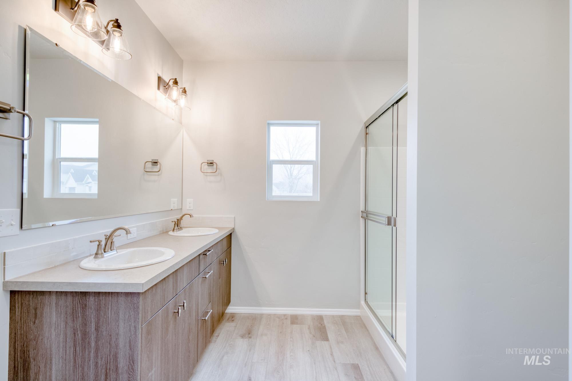 Bathroom with double vanity, plenty of natural light, light wood-style flooring, and a stall shower