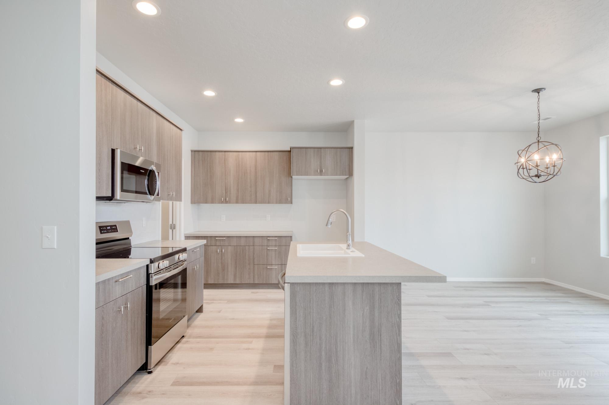 Kitchen with stainless steel appliances, modern cabinets, recessed lighting, hanging light fixtures, and an island with sink