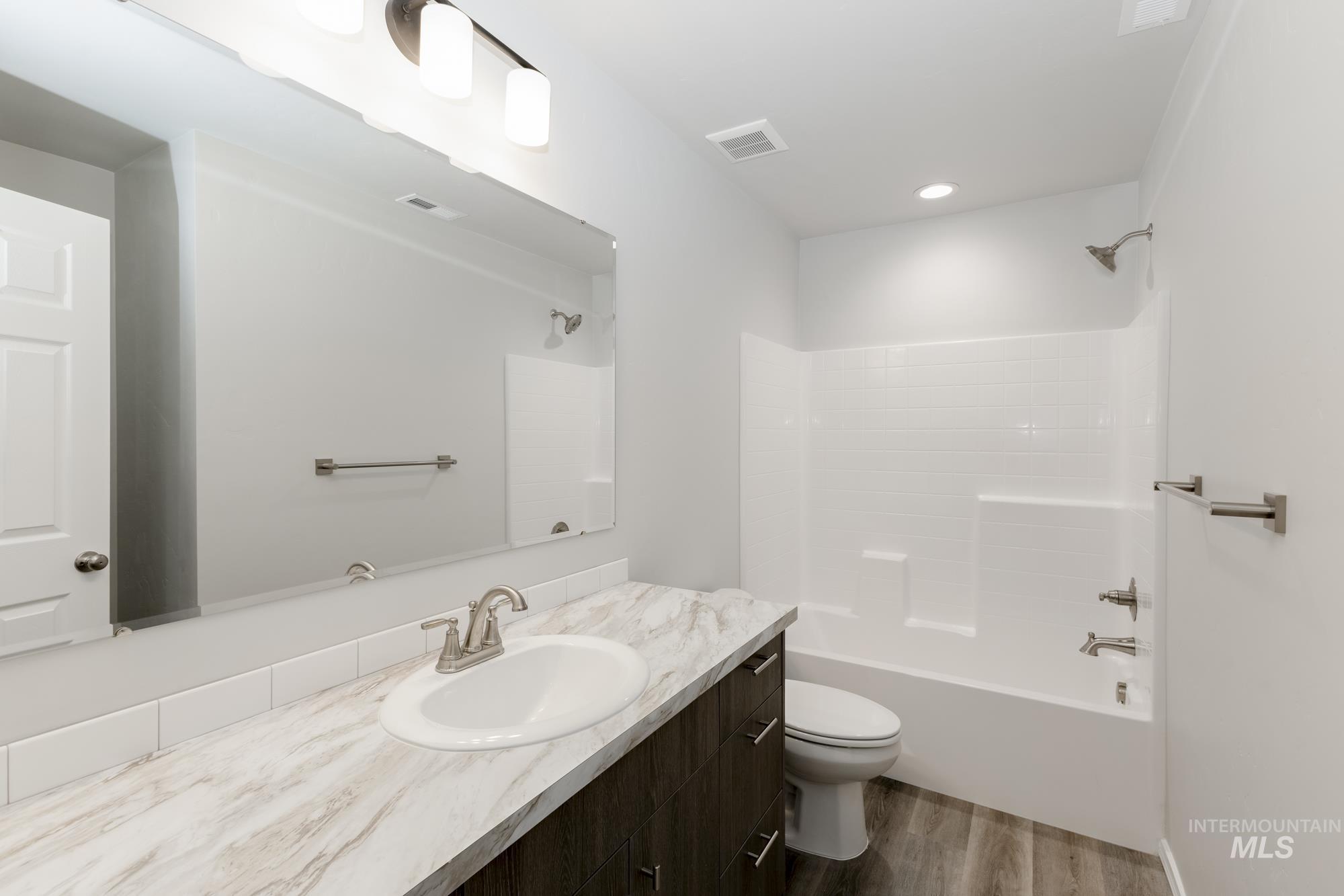 Bathroom featuring washtub / shower combination, vanity, and dark wood-type flooring