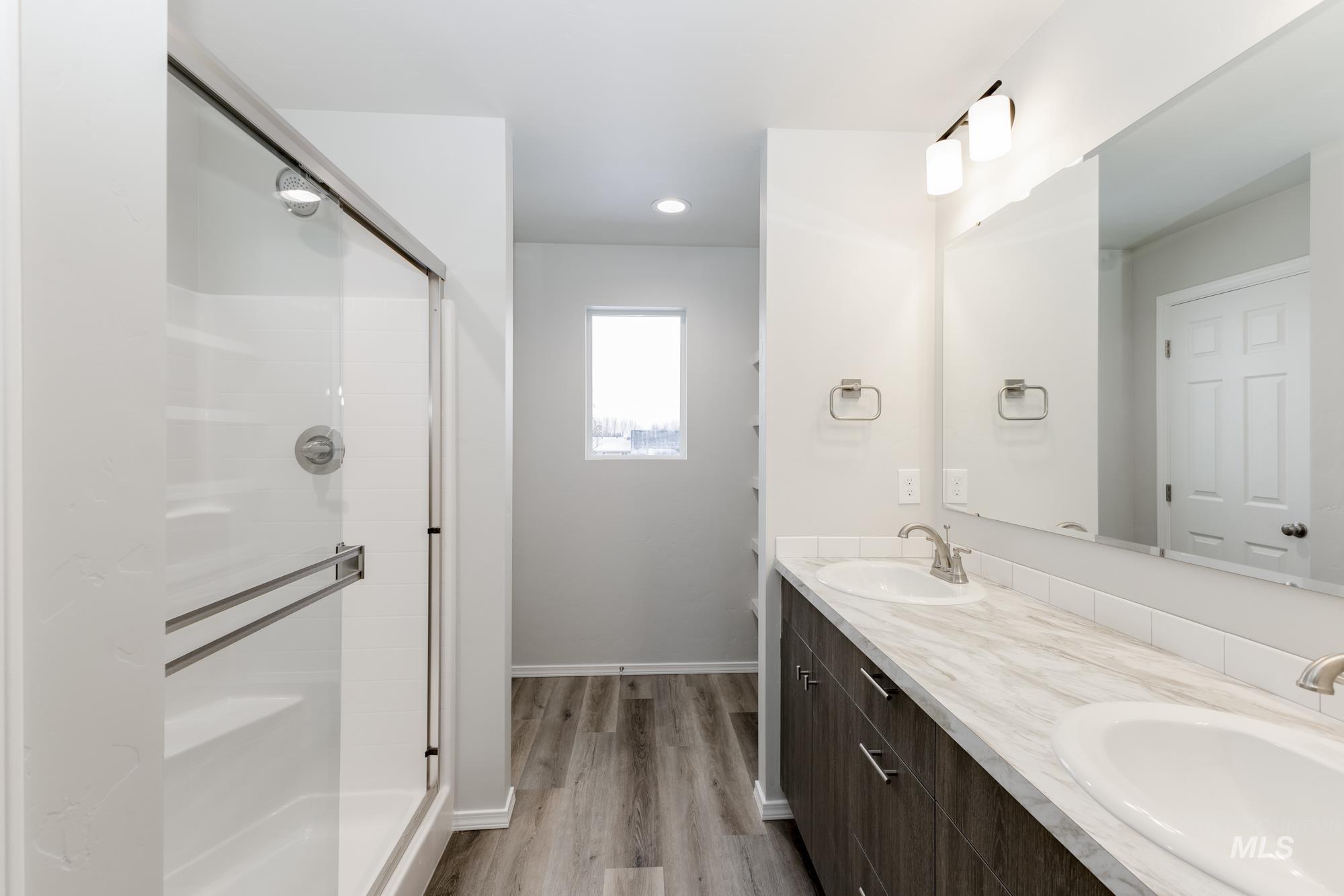 Full bathroom featuring double vanity, light wood-type flooring, a shower stall, and recessed lighting