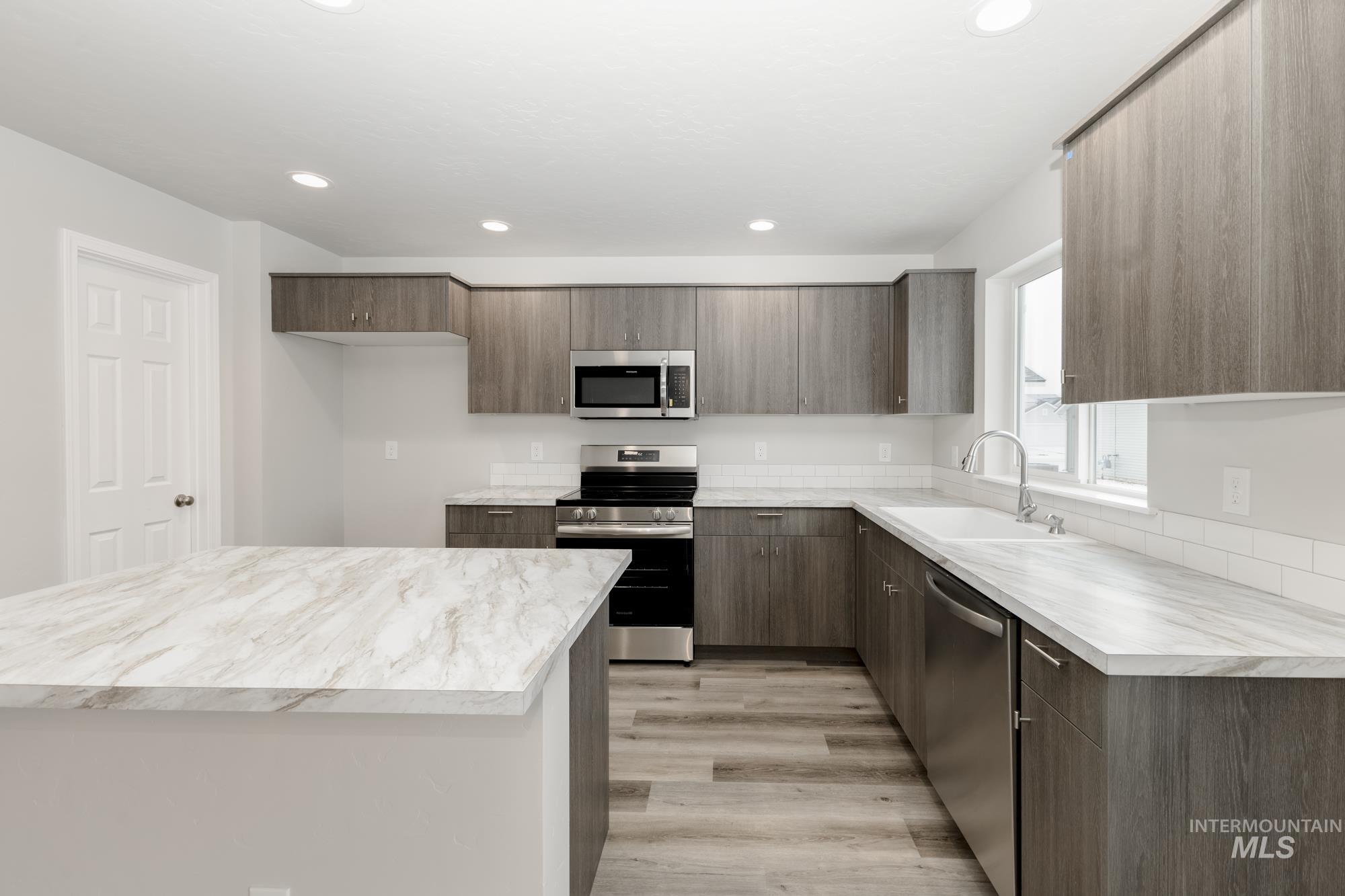 Kitchen featuring appliances with stainless steel finishes, light countertops, a kitchen island, light wood-style floors, and dark brown cabinets
