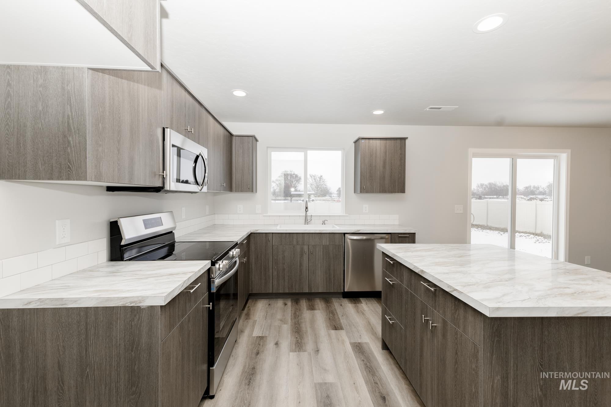 Kitchen featuring appliances with stainless steel finishes, a kitchen island, light countertops, modern cabinets, and recessed lighting