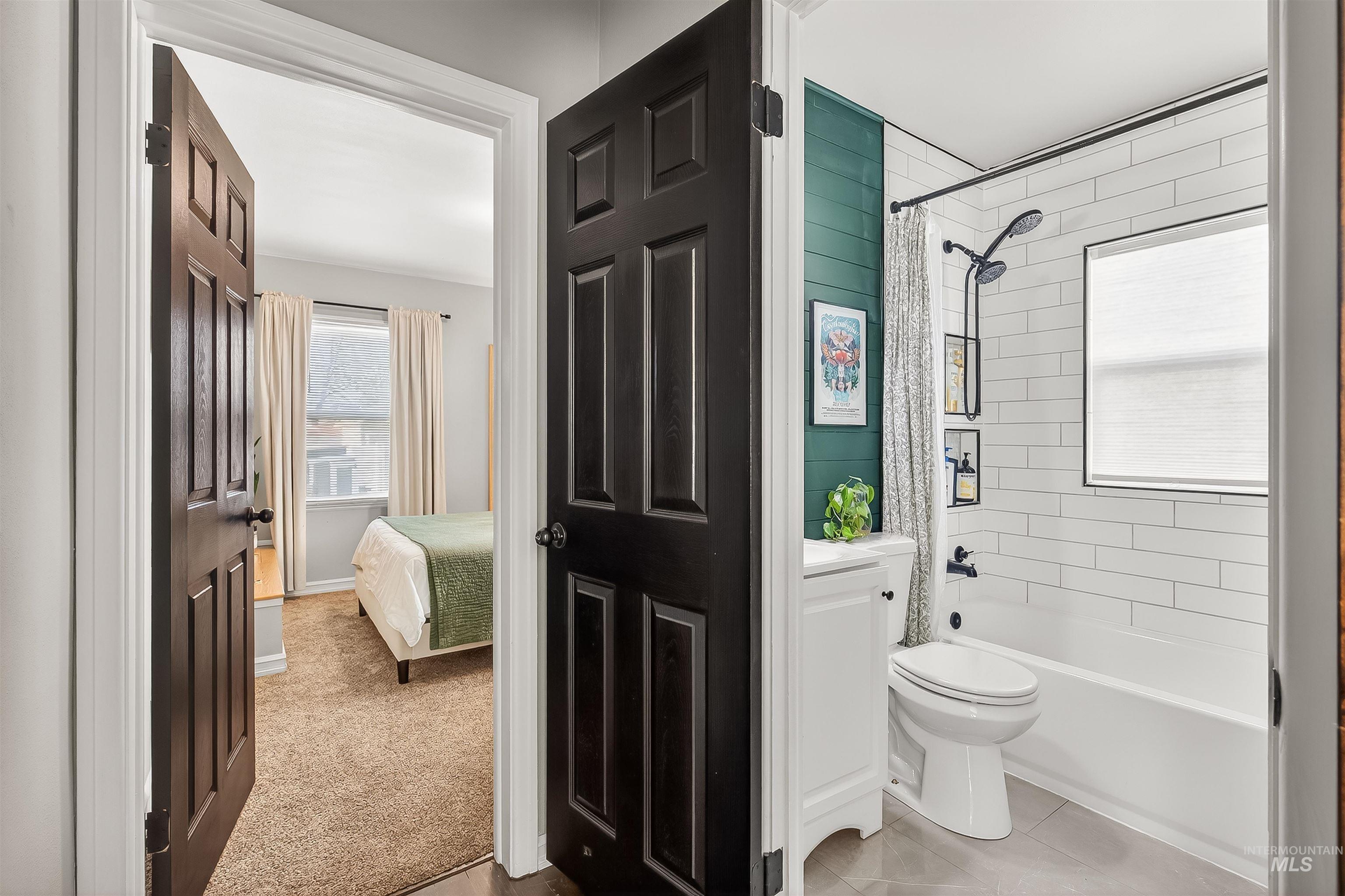 Ensuite bathroom featuring shower / bathtub combination with curtain, vanity, light tile patterned floors, and light carpet