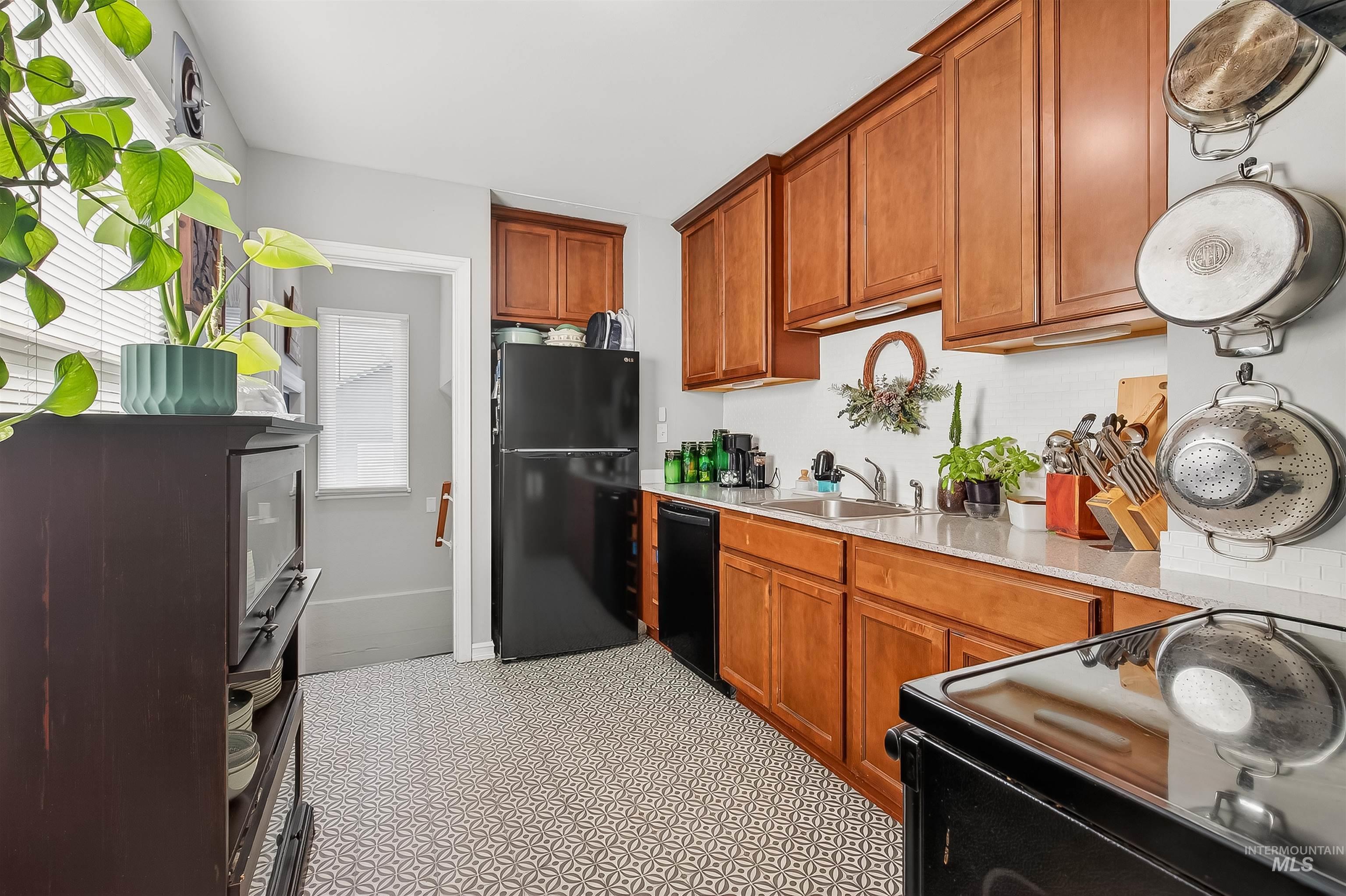 Kitchen with black appliances, brown cabinetry, and light stone countertops