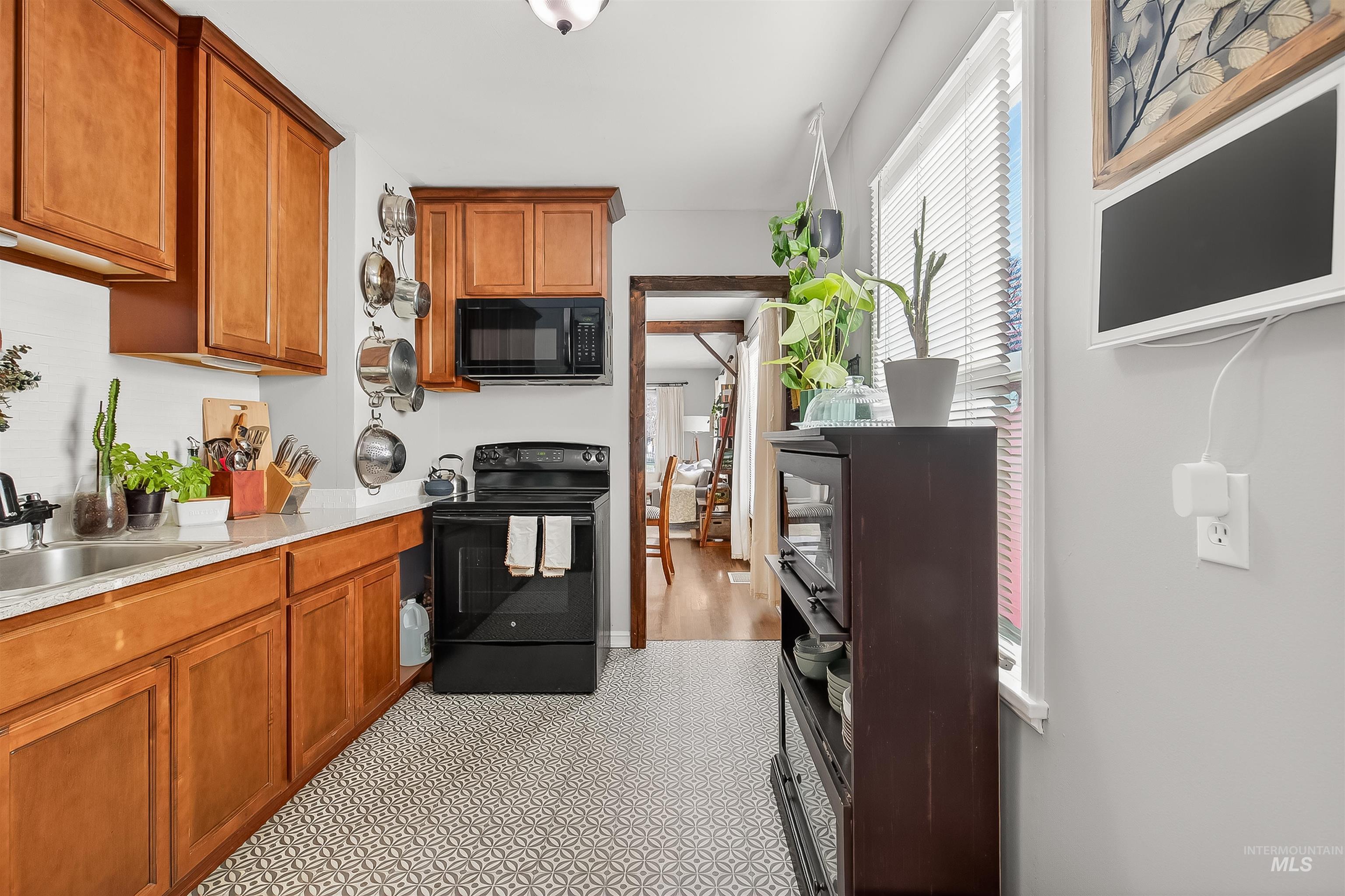 Kitchen featuring black appliances, brown cabinetry, and light stone counters