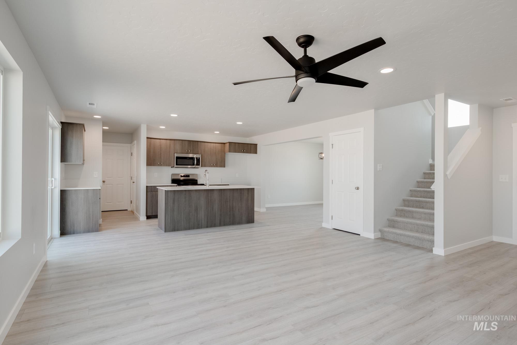 Kitchen featuring open floor plan, light countertops, ceiling fan, modern cabinets, and a center island with sink