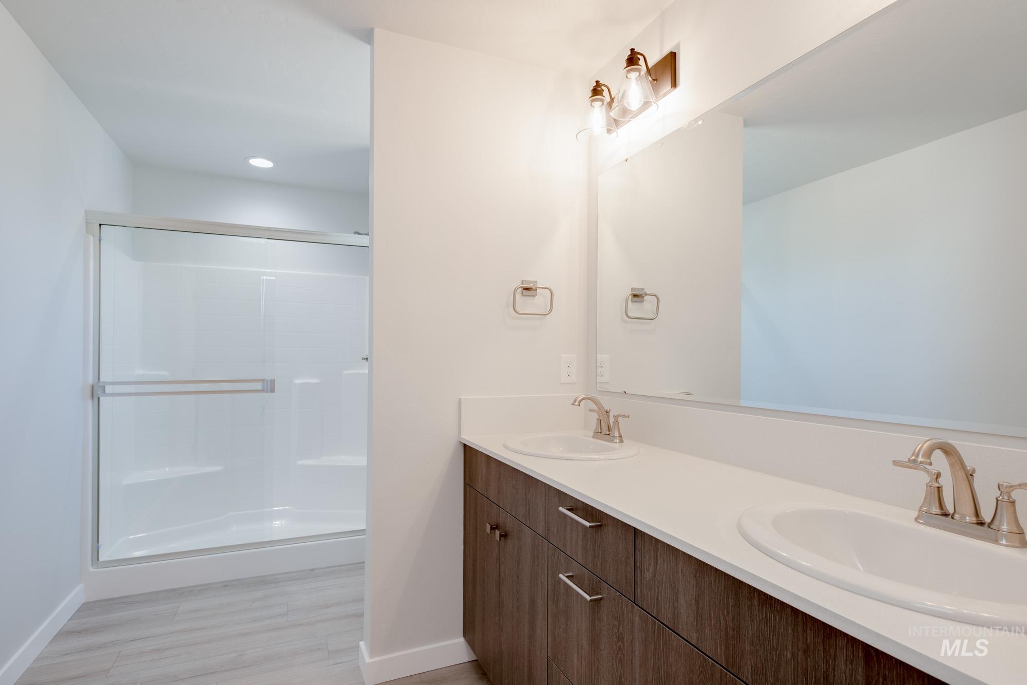 Bathroom featuring double vanity, a stall shower, and light wood-style floors