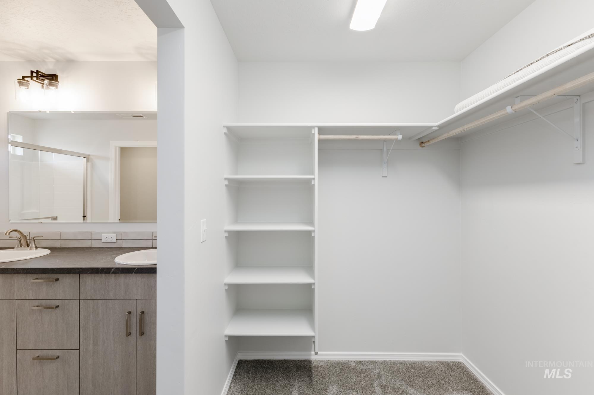 Walk in closet with dark colored carpet and a sink
