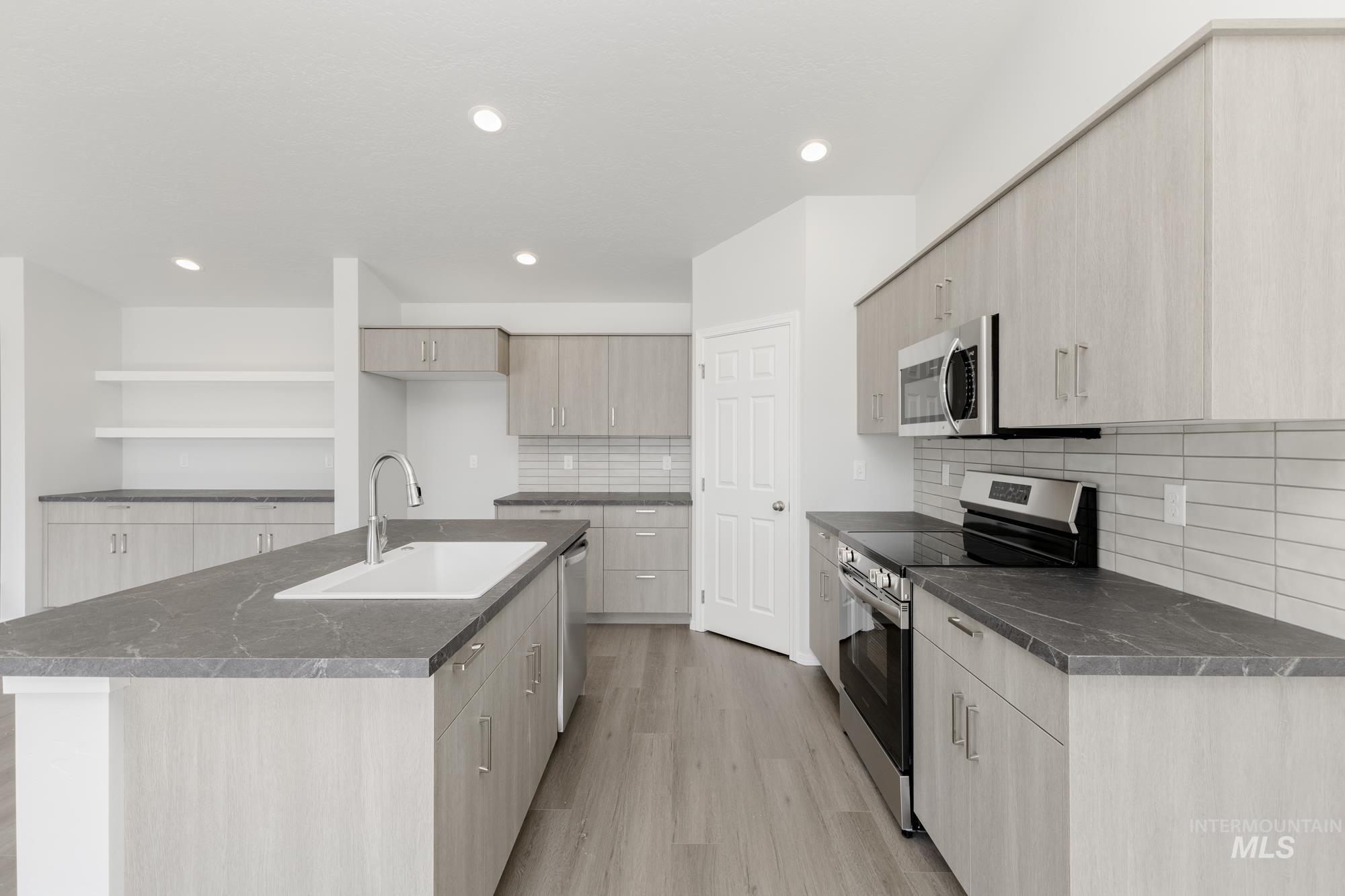Kitchen featuring appliances with stainless steel finishes, open shelves, an island with sink, decorative backsplash, and dark stone counters