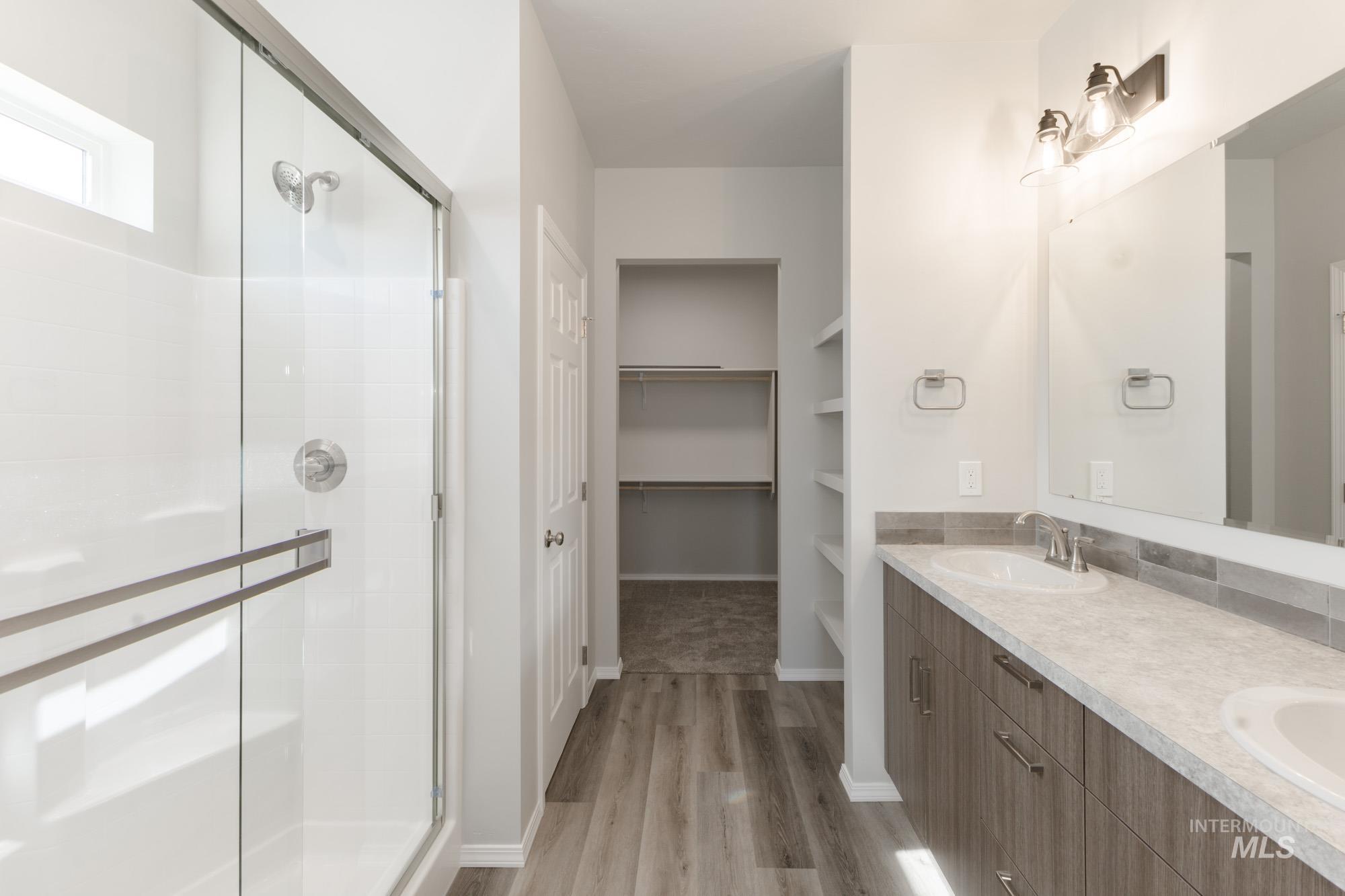 Bathroom with double vanity, a walk in closet, light wood finished floors, and a stall shower
