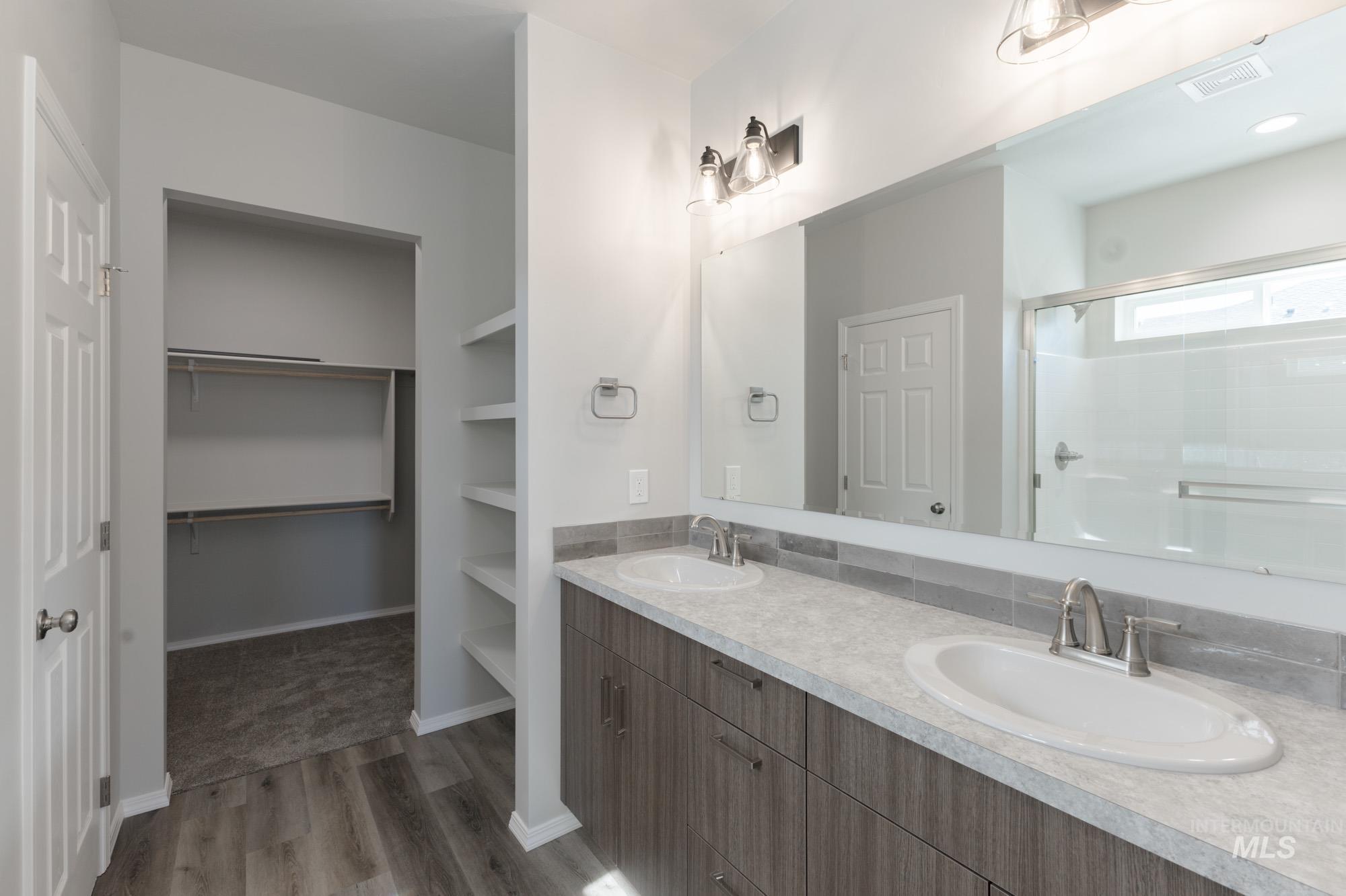 Full bath featuring double vanity, a stall shower, a walk in closet, and light wood-type flooring
