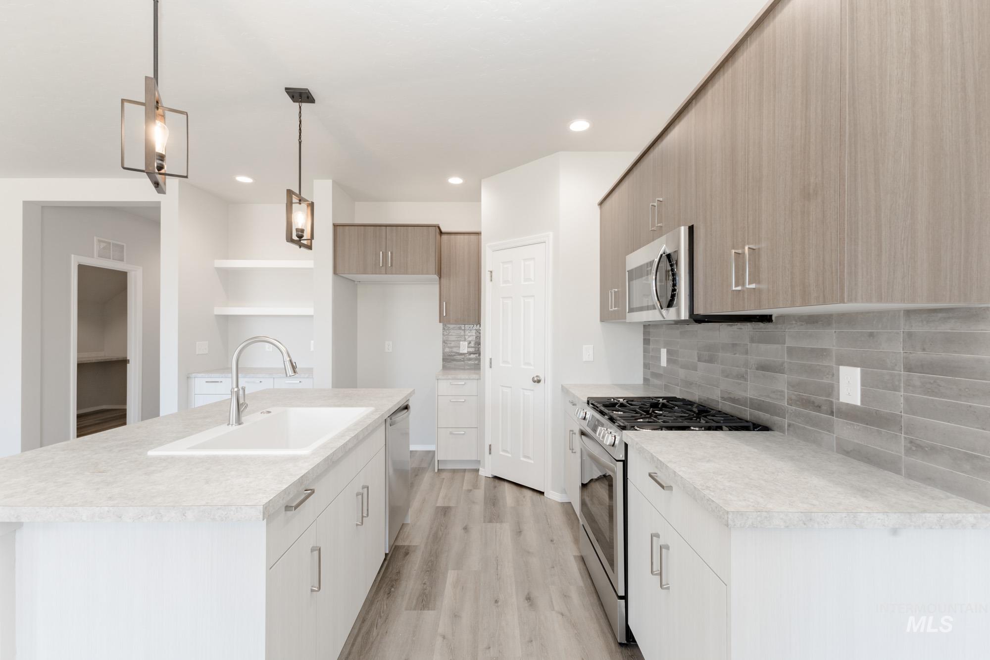 Kitchen with appliances with stainless steel finishes, light countertops, decorative light fixtures, tasteful backsplash, and light wood-style floors