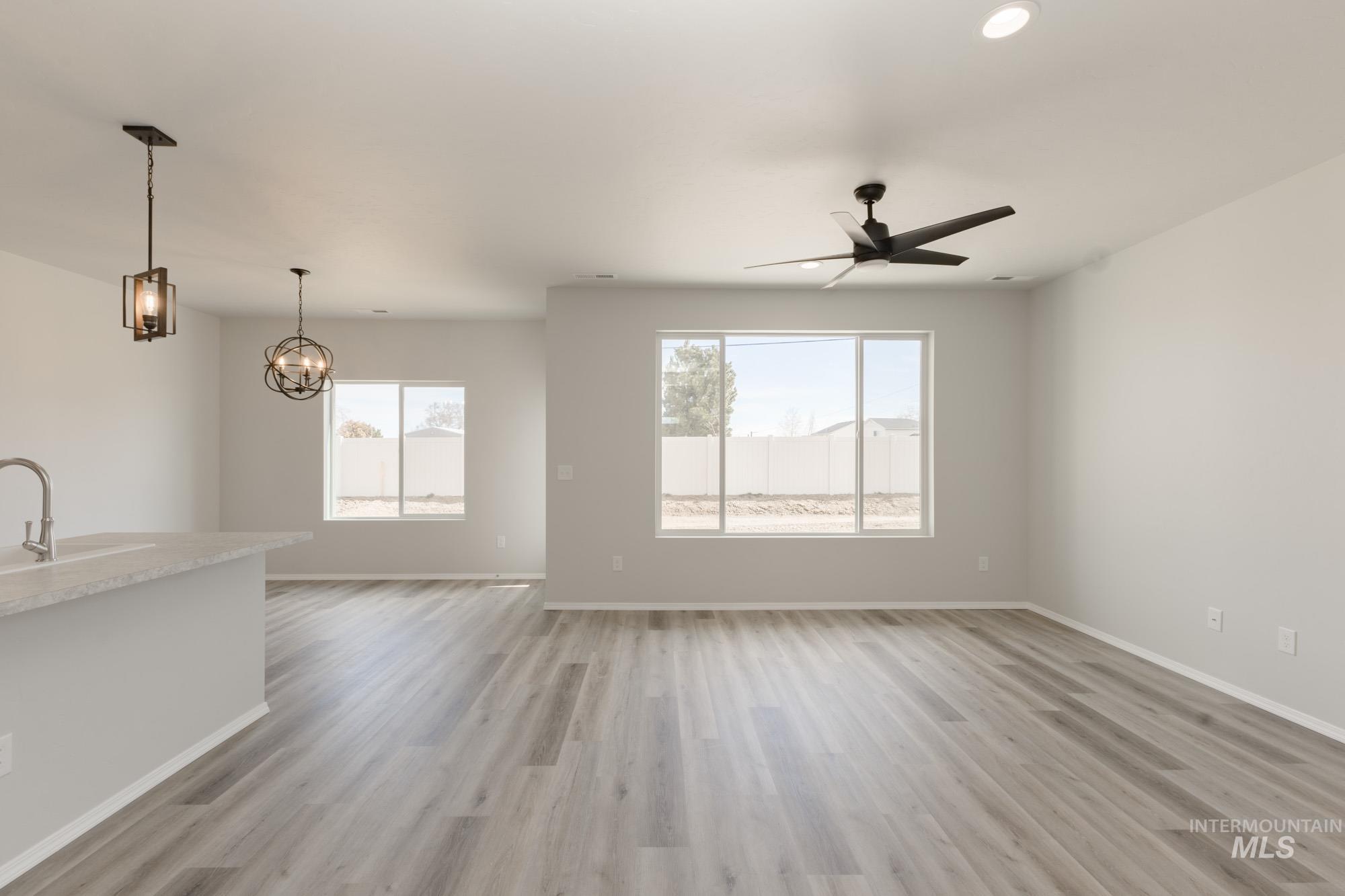Unfurnished living room with light wood-style flooring, plenty of natural light, a ceiling fan, and a chandelier