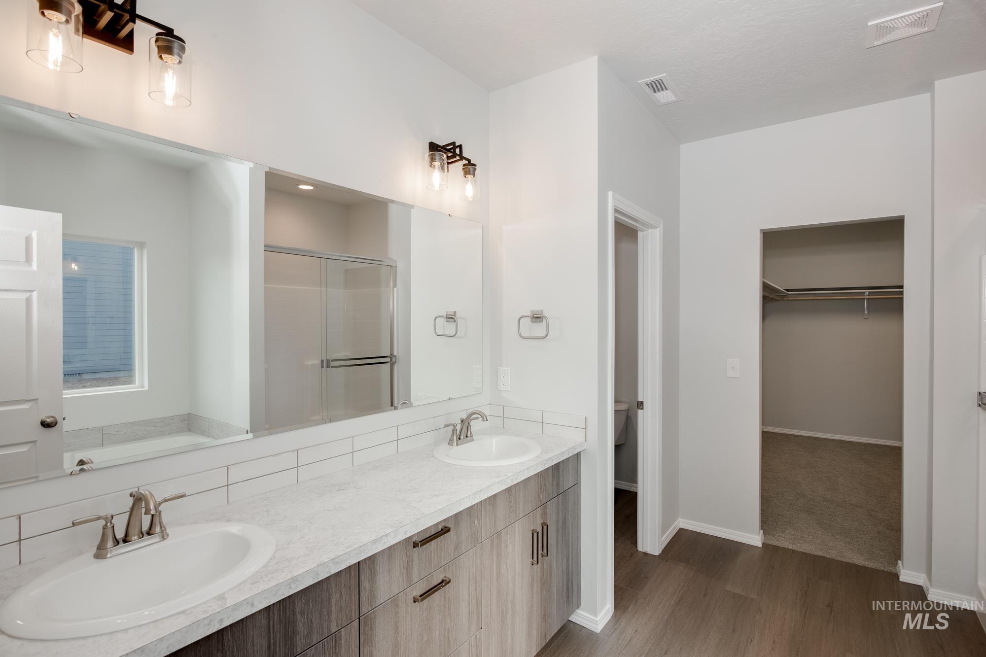 Bathroom featuring a spacious closet, a shower stall, double vanity, dark wood-style flooring, and a bath