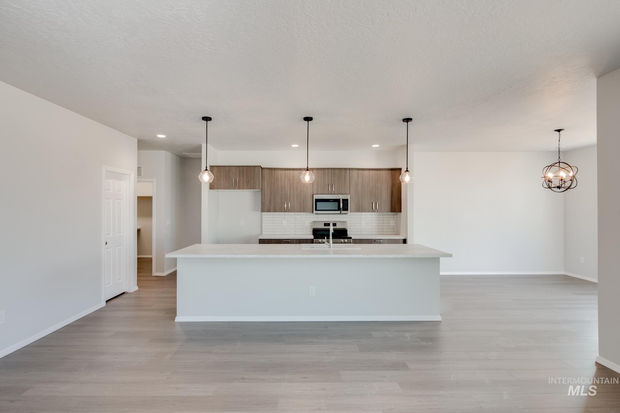Kitchen with decorative light fixtures, brown cabinetry, a center island with sink, recessed lighting, and a chandelier