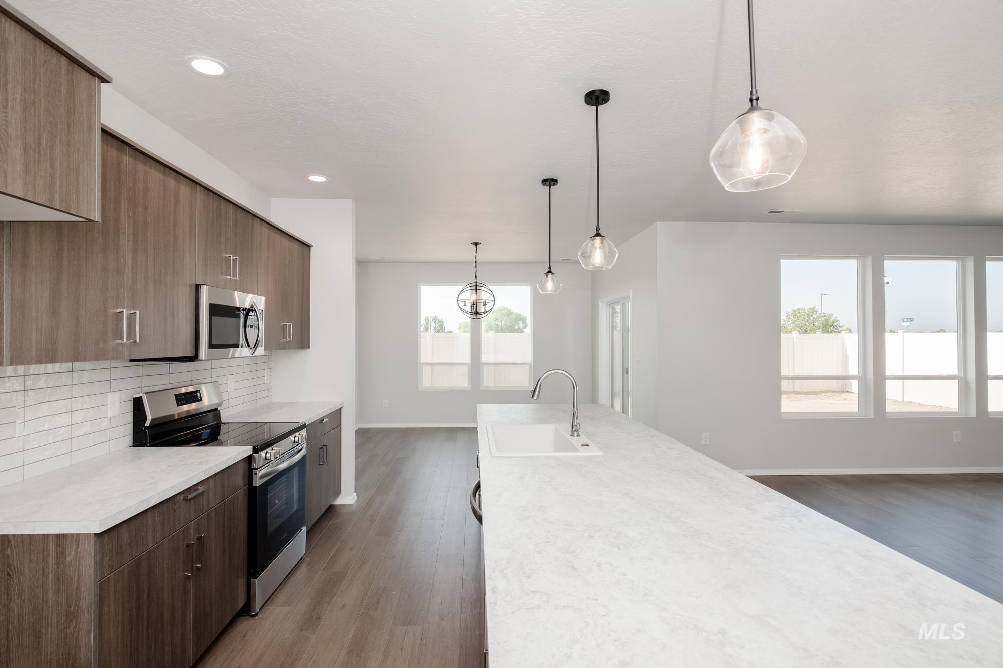 Kitchen featuring appliances with stainless steel finishes, hanging light fixtures, backsplash, dark wood-type flooring, and modern cabinets